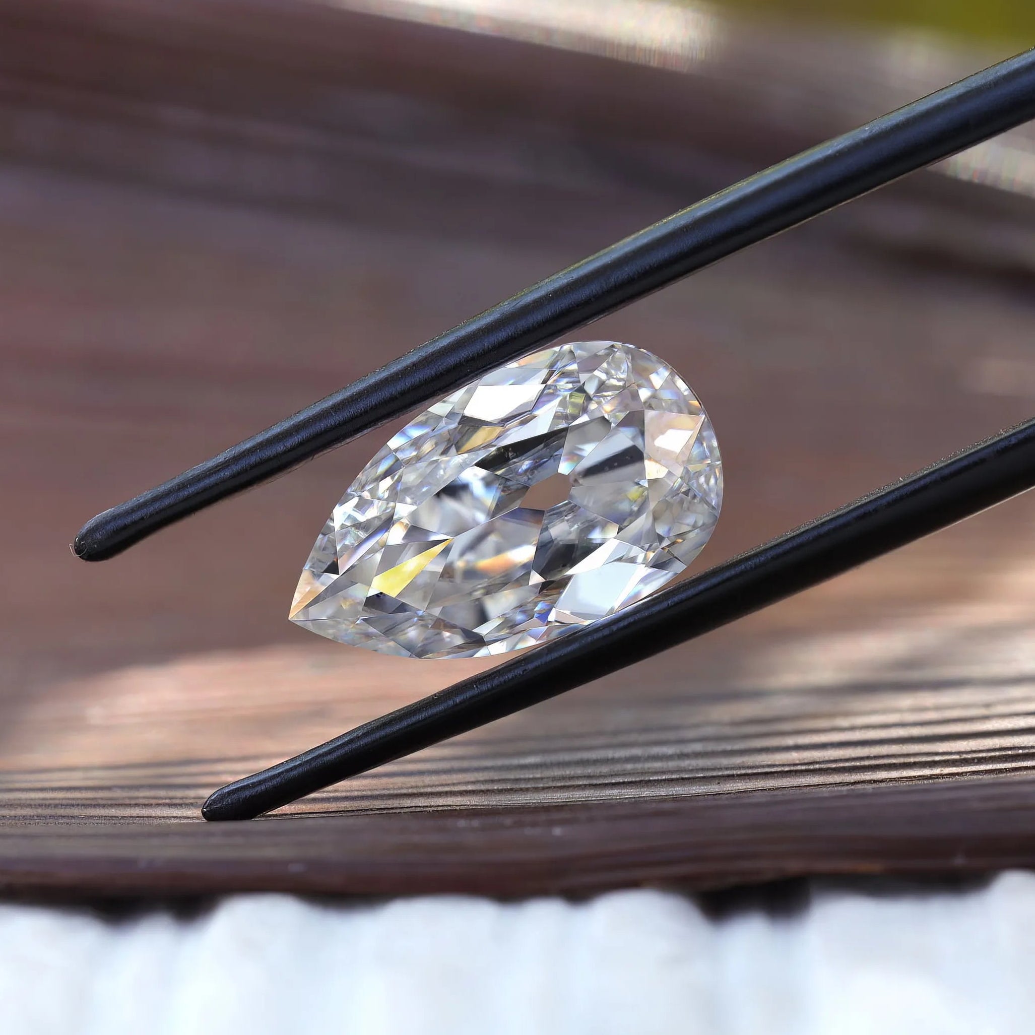 Horizontal pear old mine cut moissanite in tweezers