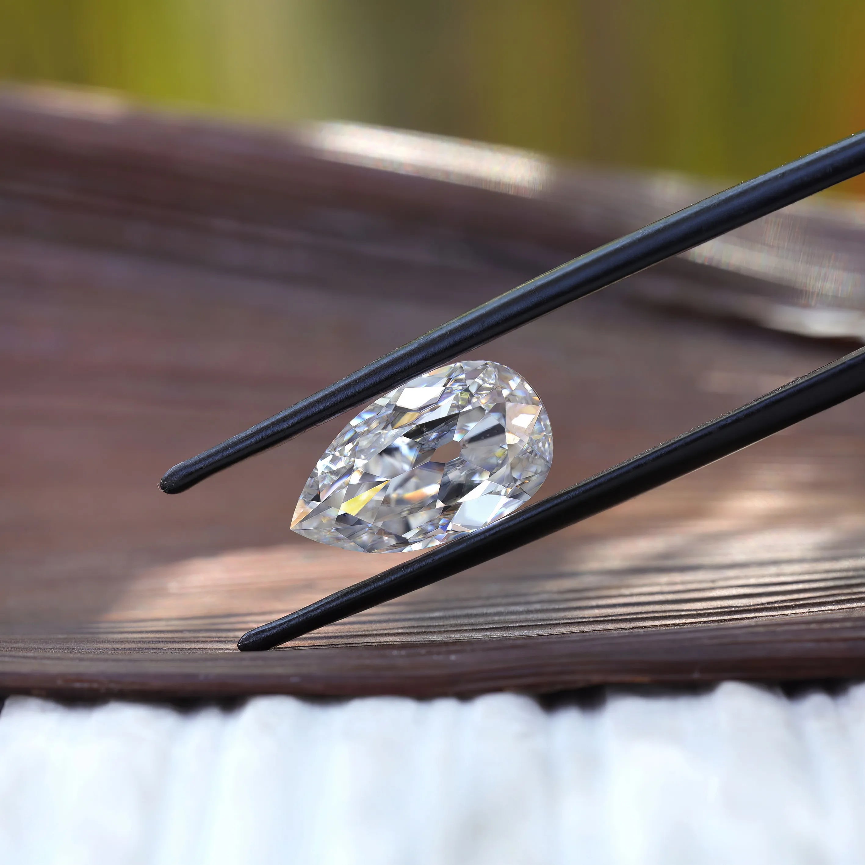 Horizontal pear old mine cut moissanite in tweezers