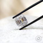 Emerald step cut moissanite displayed in black tweezers close-up