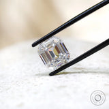 Emerald step cut moissanite displayed in black tweezers close-up