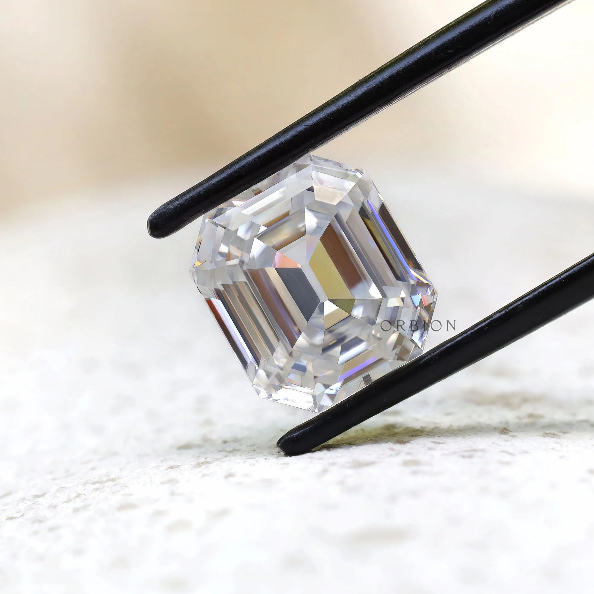 Emerald step cut moissanite displayed in black tweezers close-up
