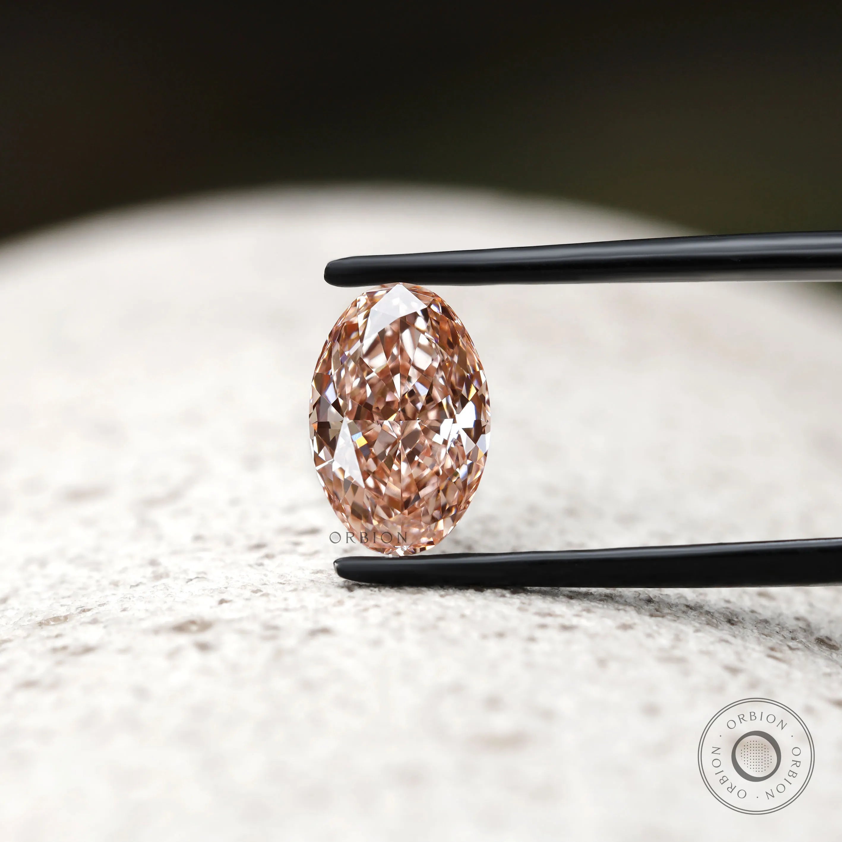 Oval pink lab diamond displayed on textured neutral background