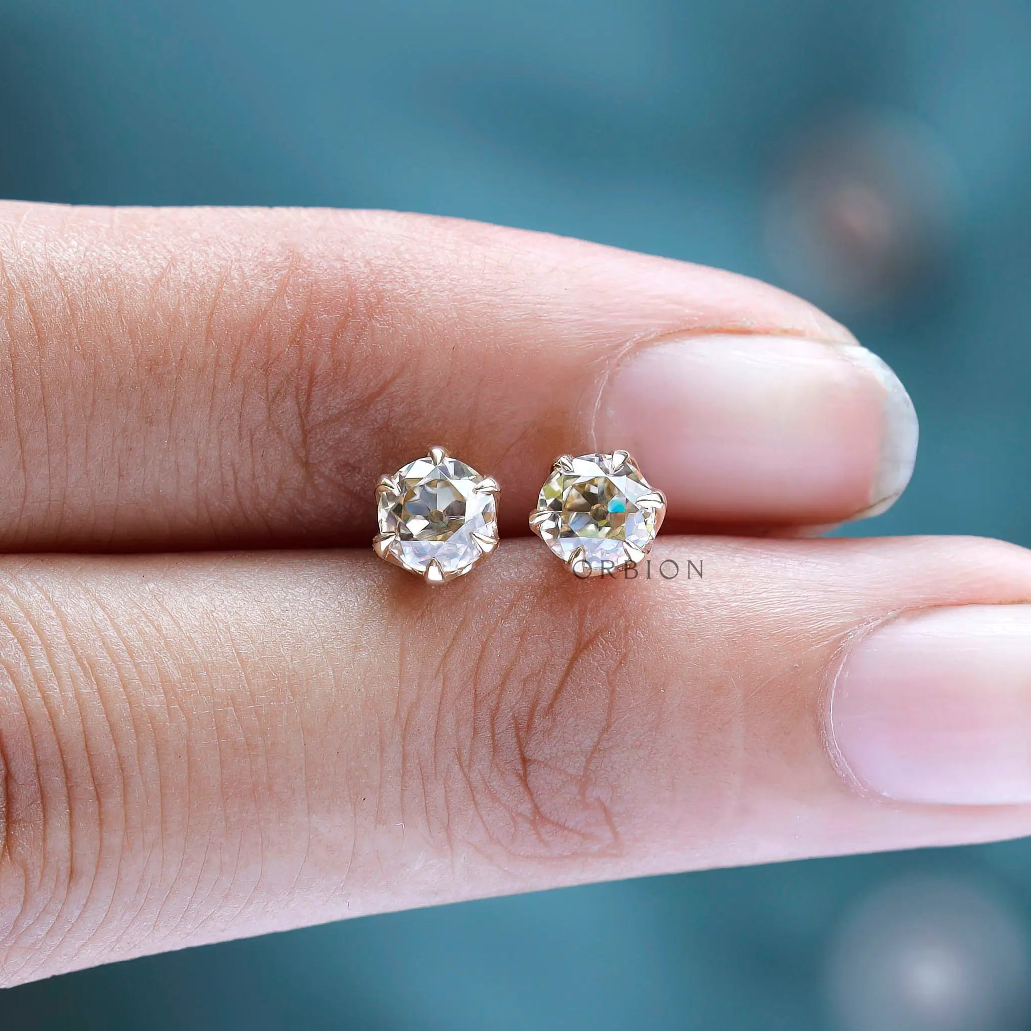 Hand scale view small champagne moissanite stud earrings gold