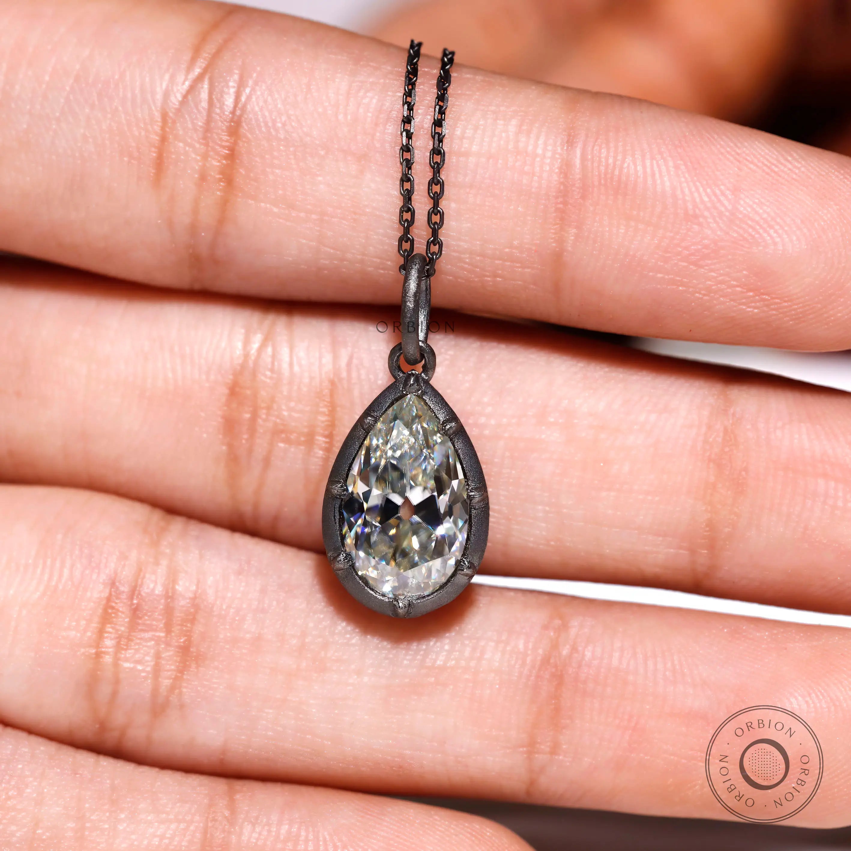 Pear moissanite pendant shown on hand for size reference