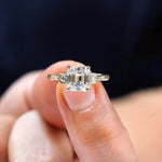 Close-up of three stone asscher moissanite engagement ring with floral motifs