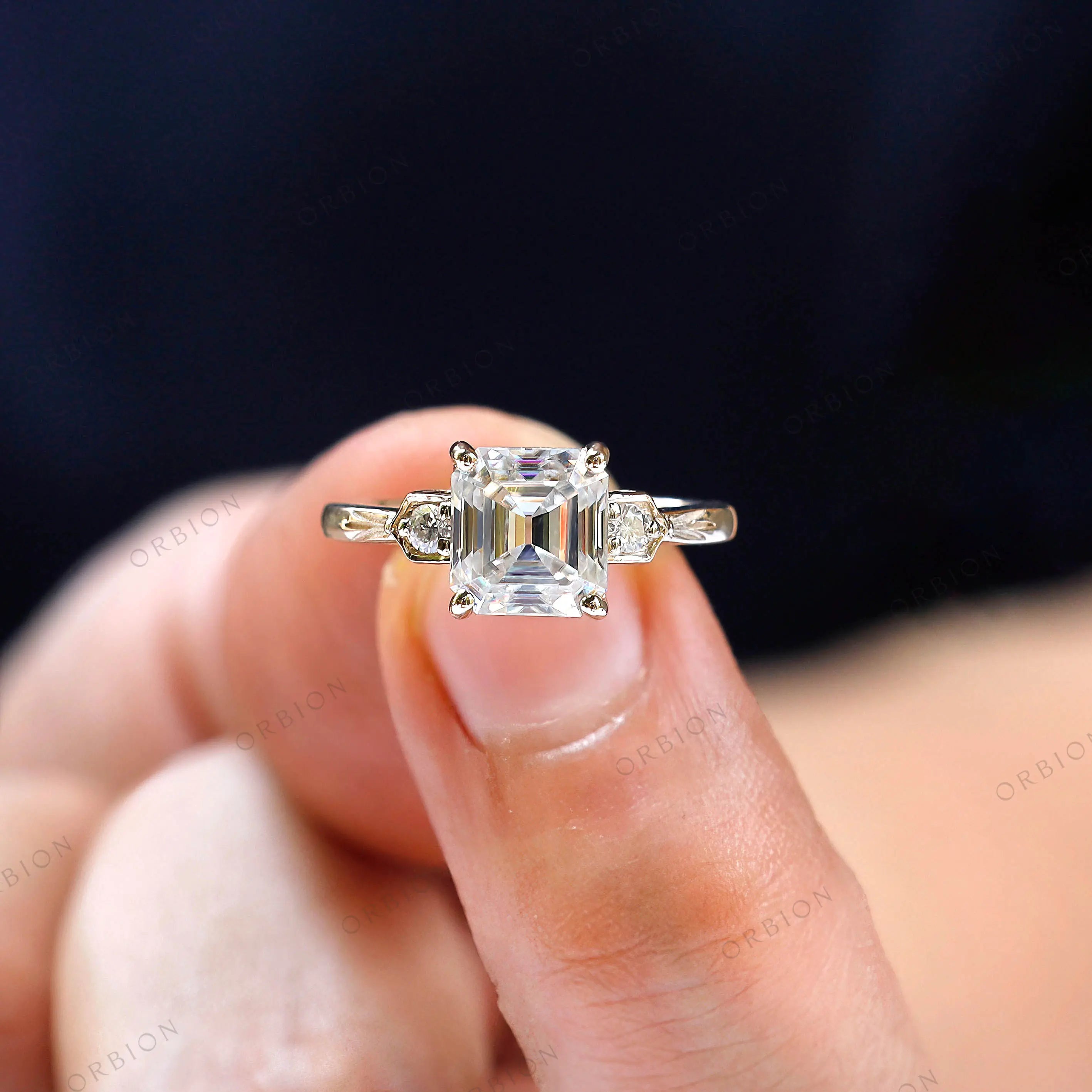 Close-up of three stone asscher moissanite engagement ring with floral motifs