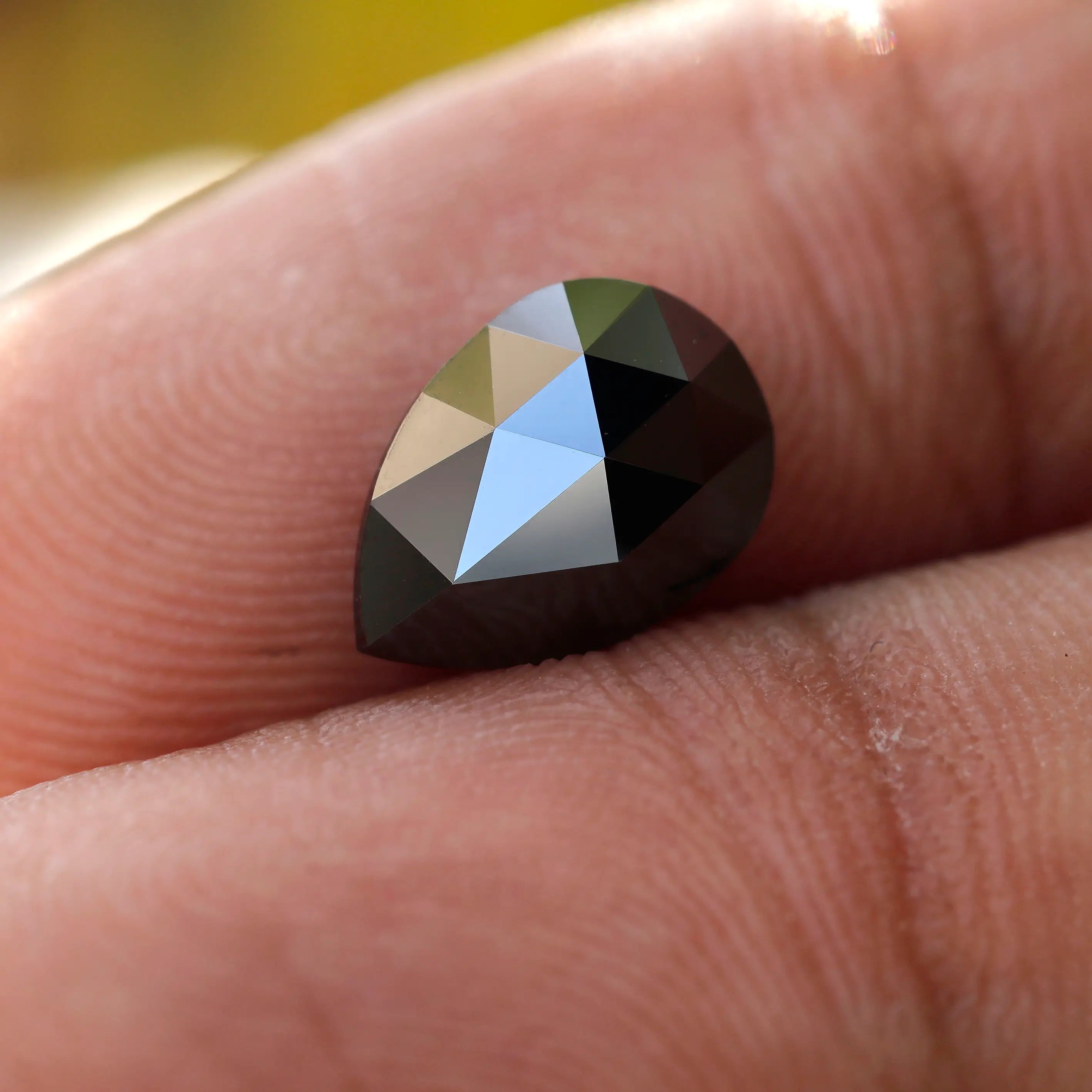 Black pear-shaped moissanite stone held between fingers