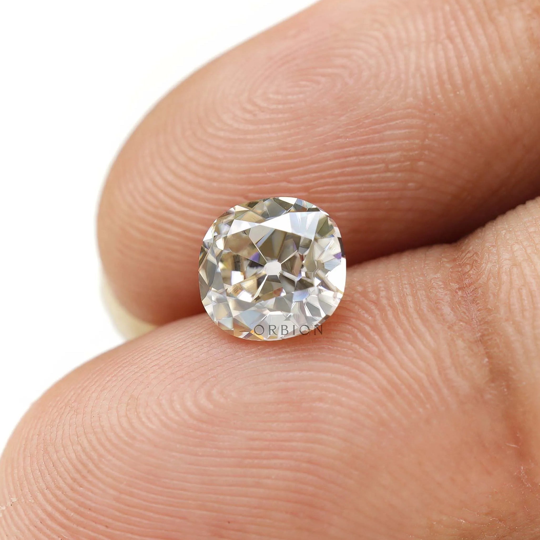 Elongated cushion loose moissanite shown on fingertips for scale
