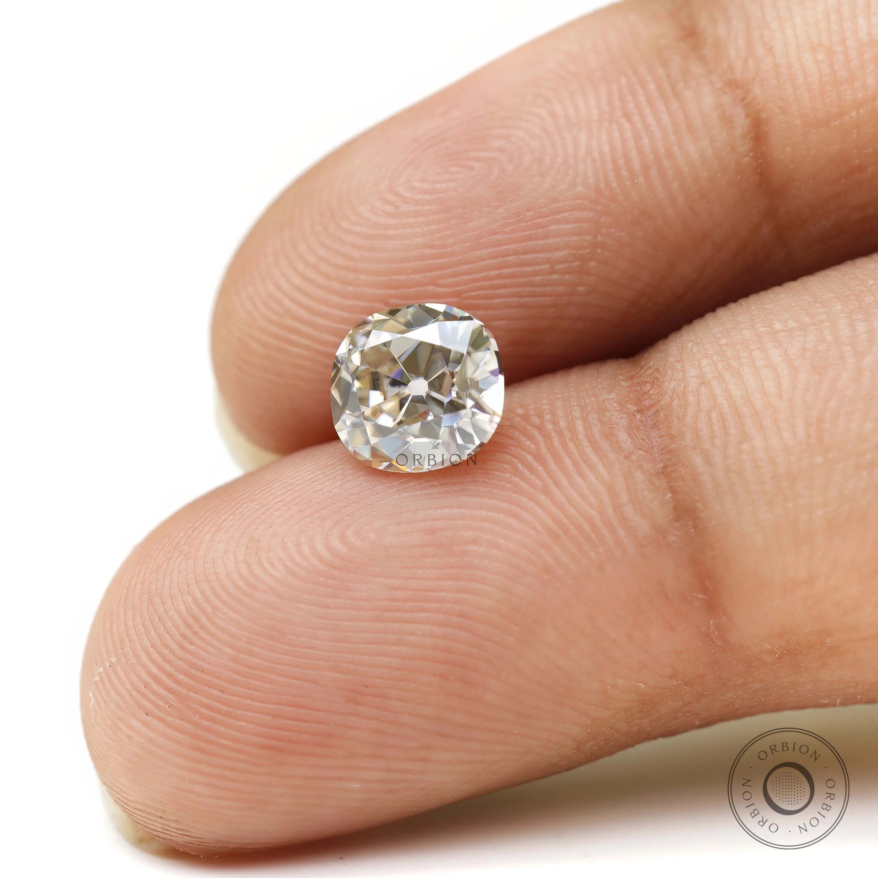 Elongated cushion loose moissanite shown on fingertips for scale