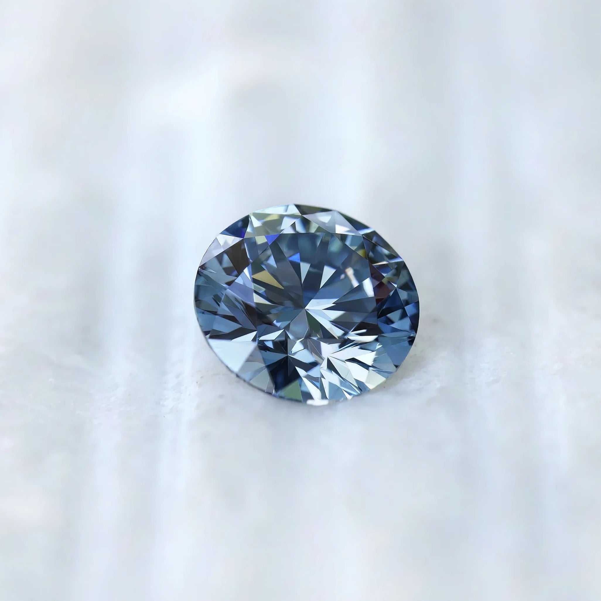 Round blue lab diamond displayed on soft white surface