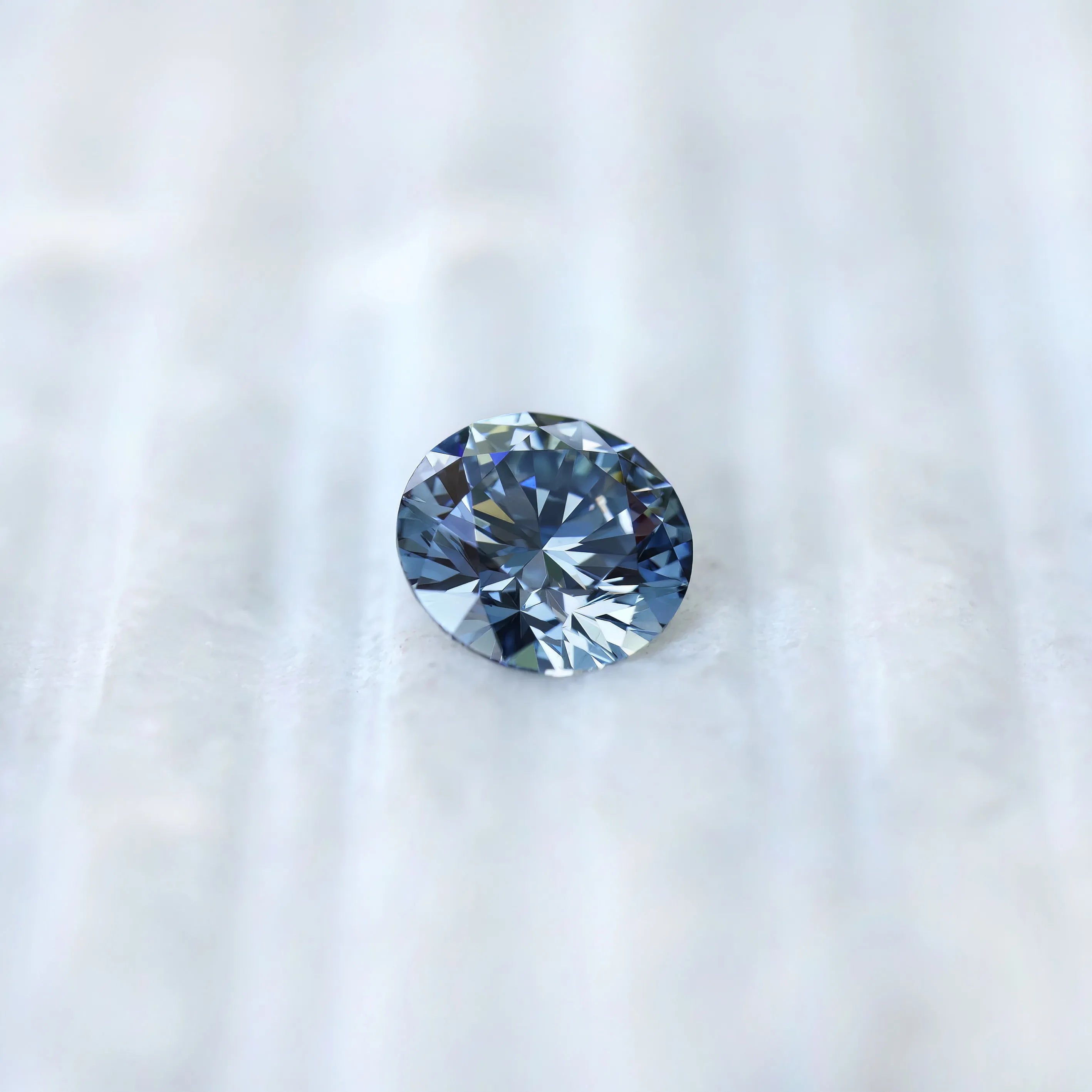 Round blue lab diamond displayed on soft white surface