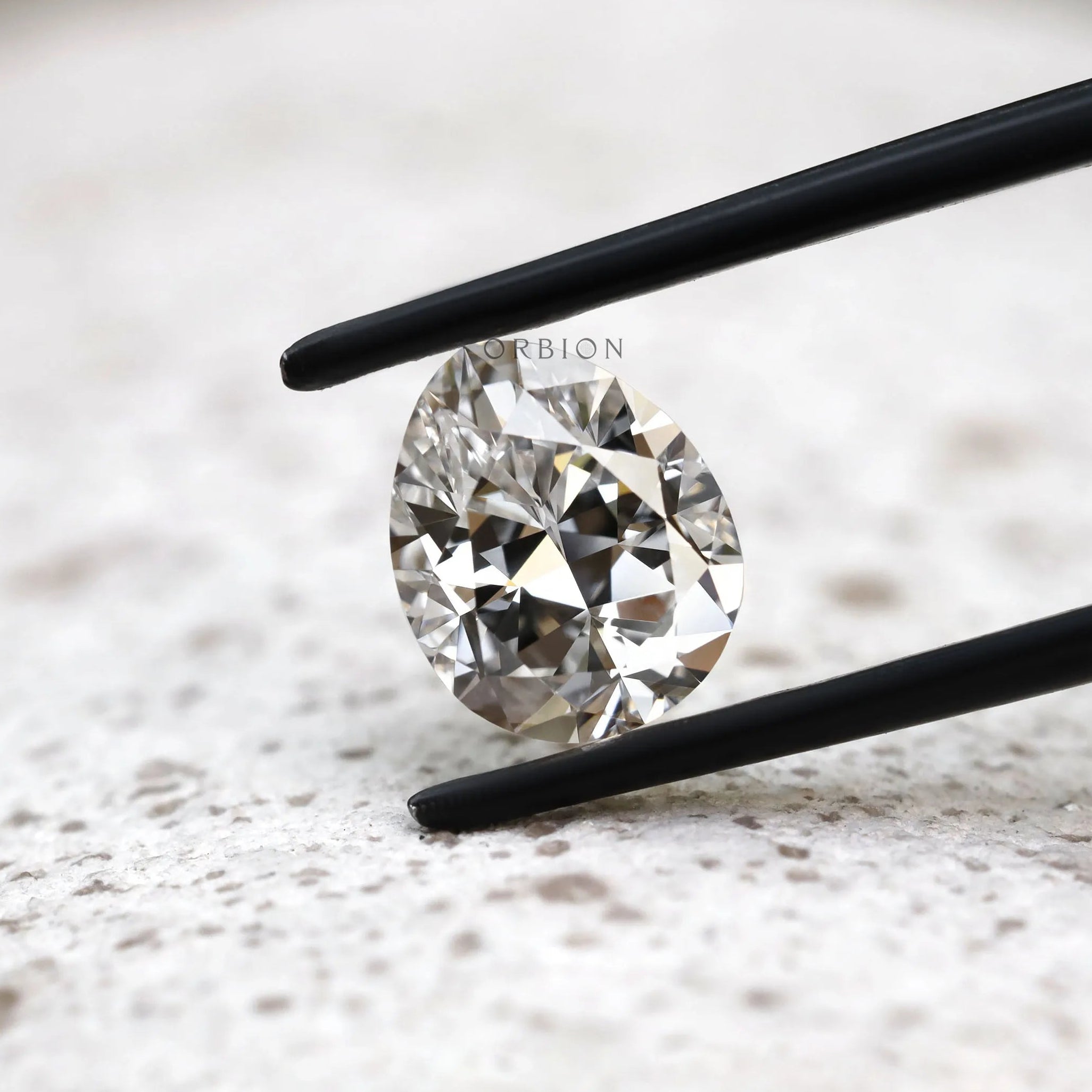 Close view of DEF pear lab diamond held between black tweezers 