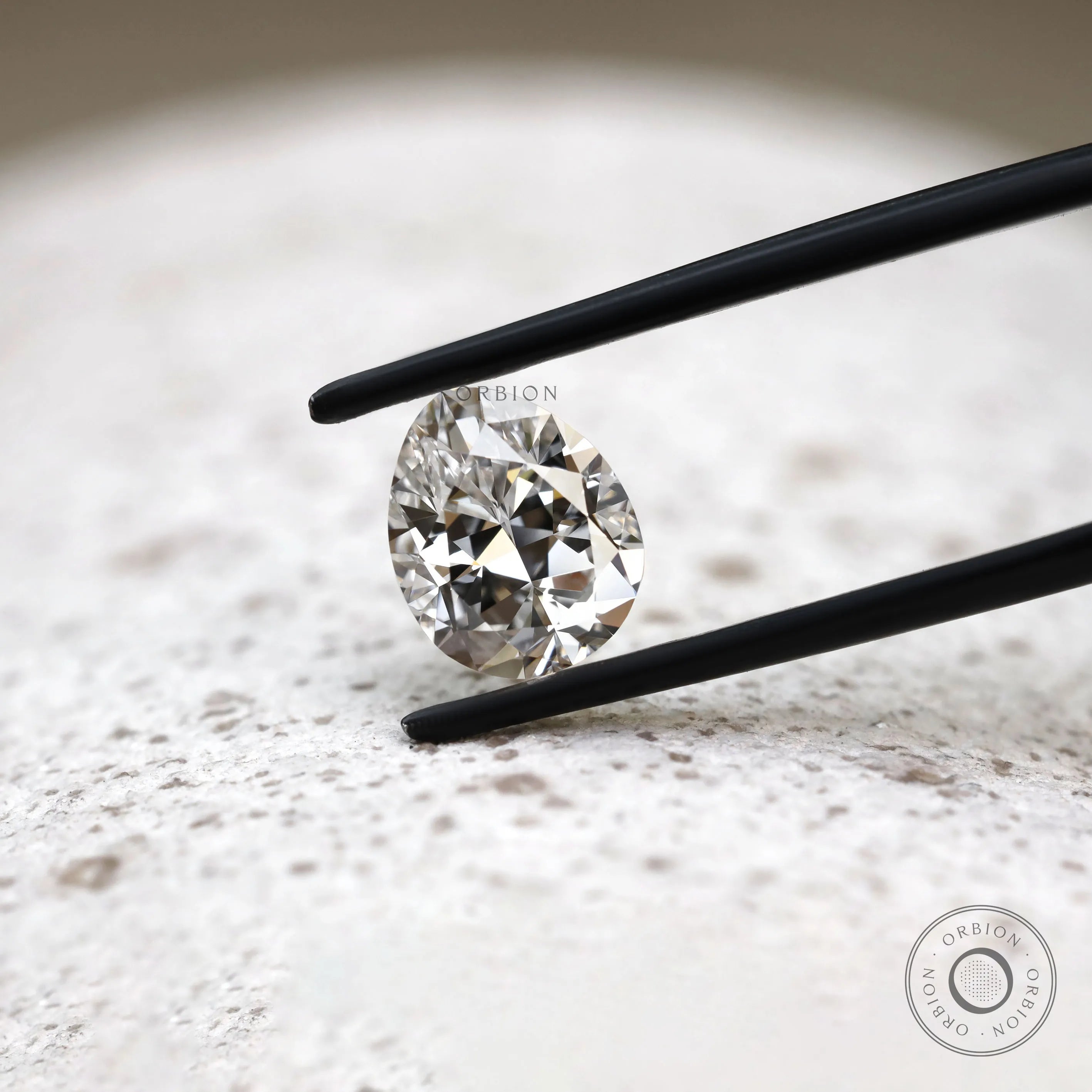 Close view of DEF pear lab diamond held between black tweezers 