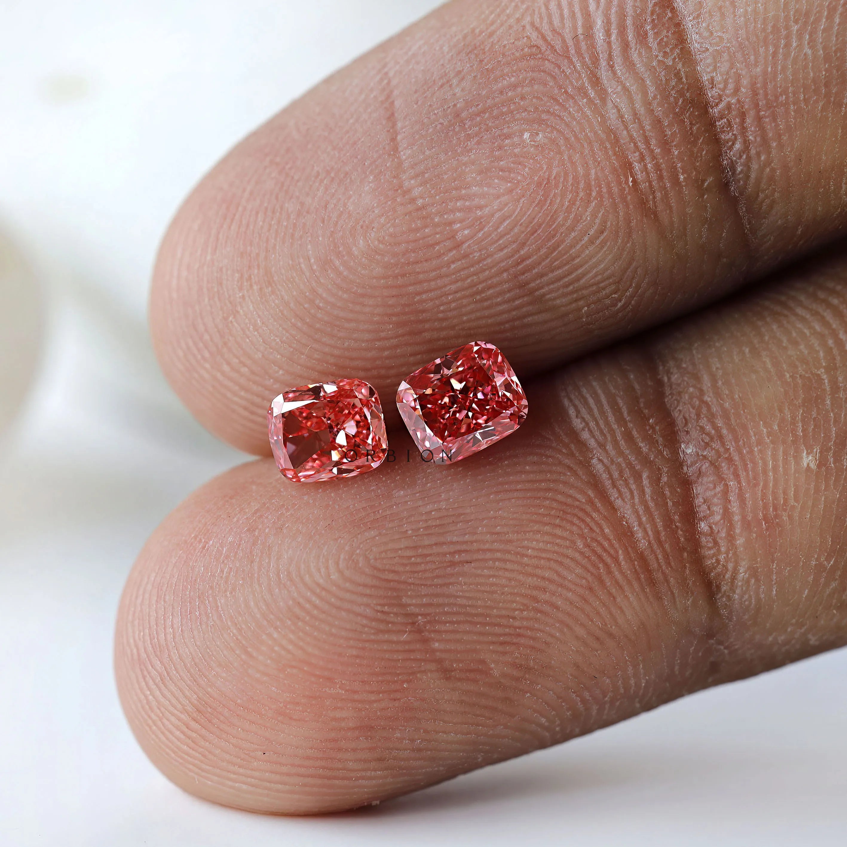 Fancy vivid pink cushion diamond pair on fingertip display