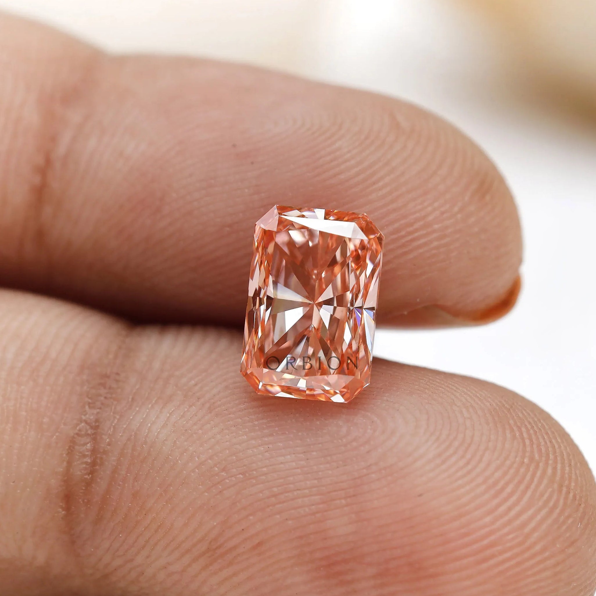 Close fingertip view of fancy pink radiant lab diamond