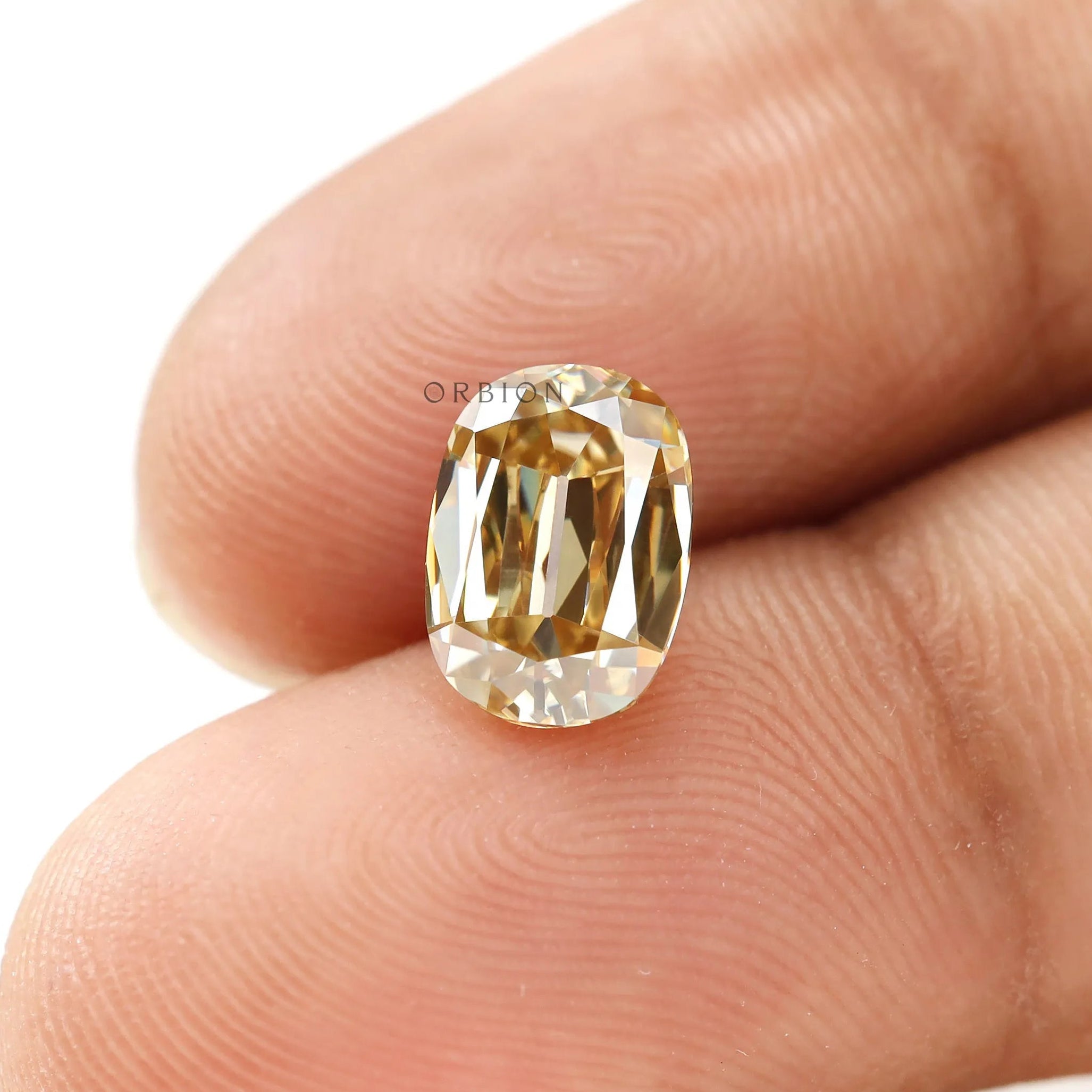 Champagne moissanite shown on fingertips in elongated cushion shape