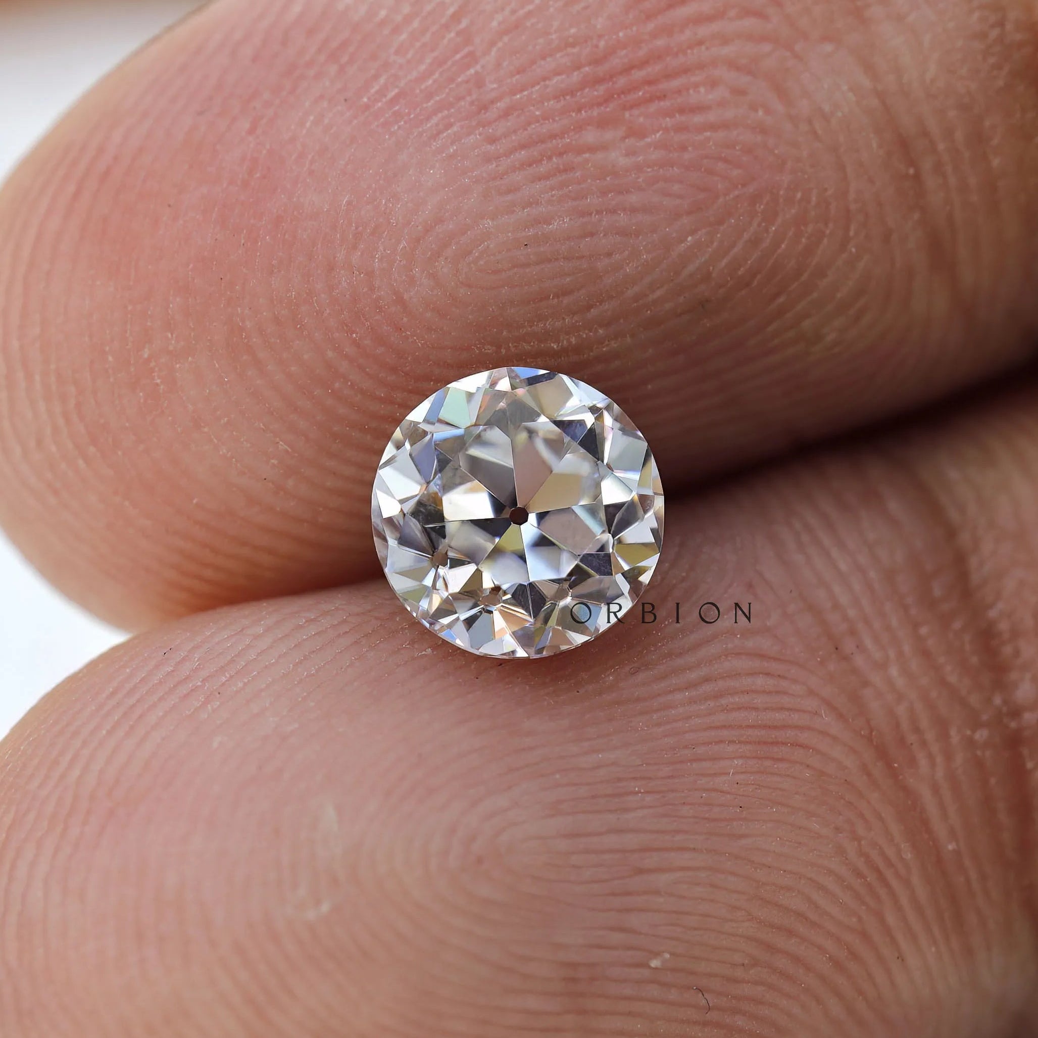 Round loose moissanite placed on fingertips for size reference