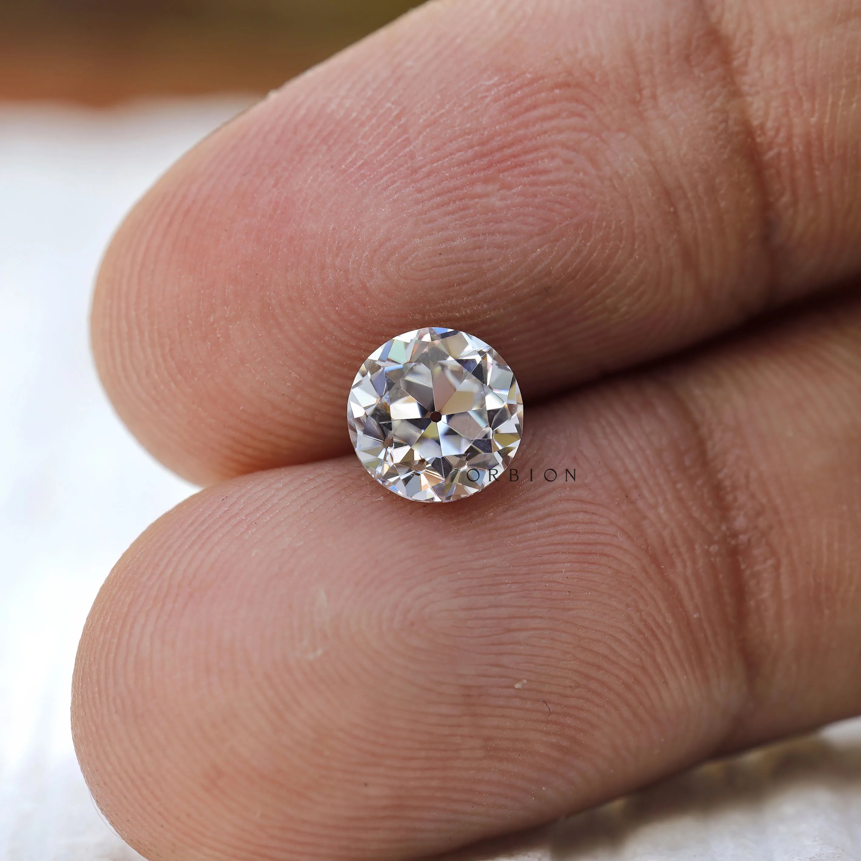 Round loose moissanite placed on fingertips for size reference