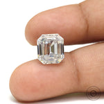 Emerald step cut moissanite shown between fingertips for scale