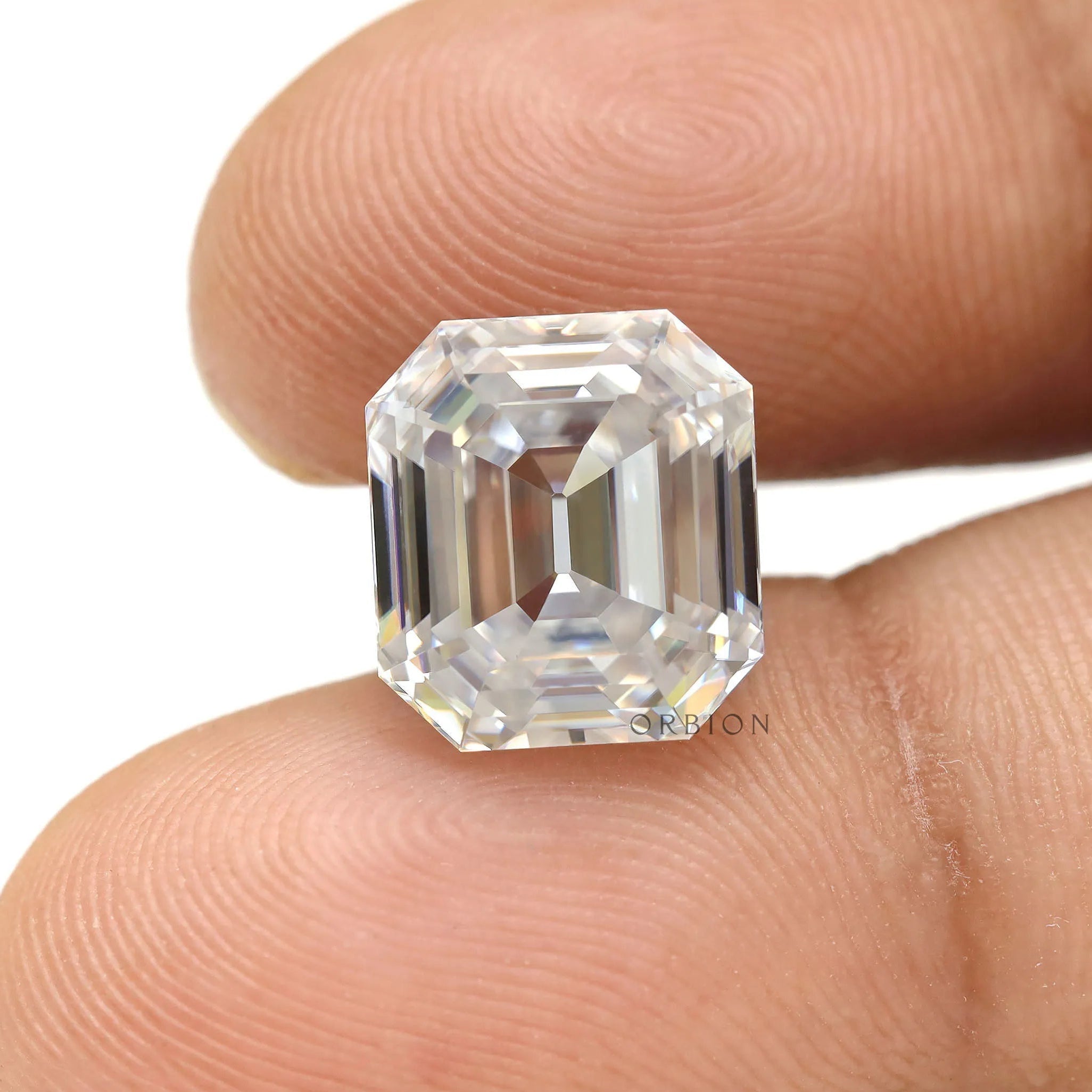 Emerald step cut moissanite shown between fingertips for scale