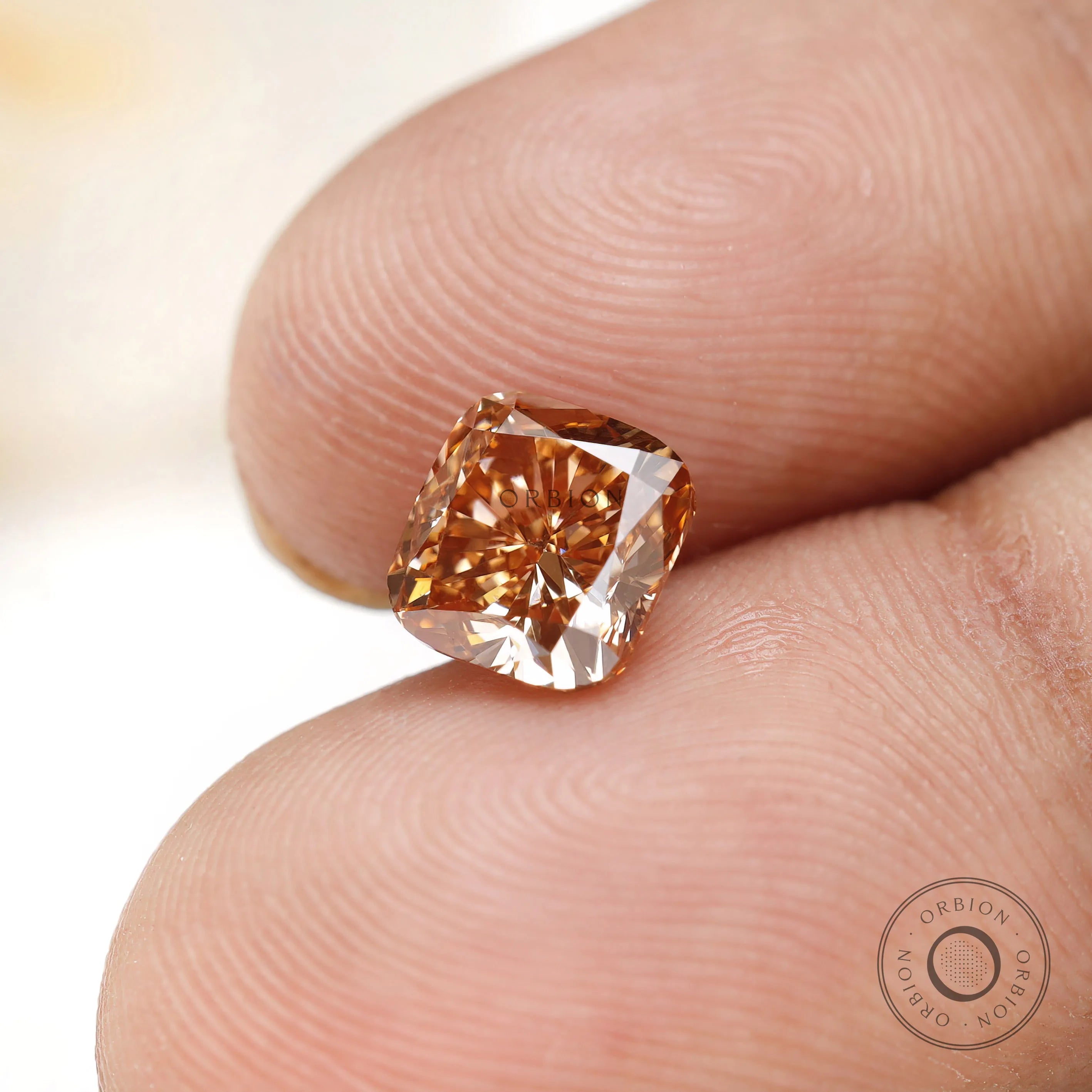 Fancy orange cushion lab diamond displayed on fingertips
