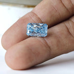 Blue radiant brilliant loose diamond shown on fingertip