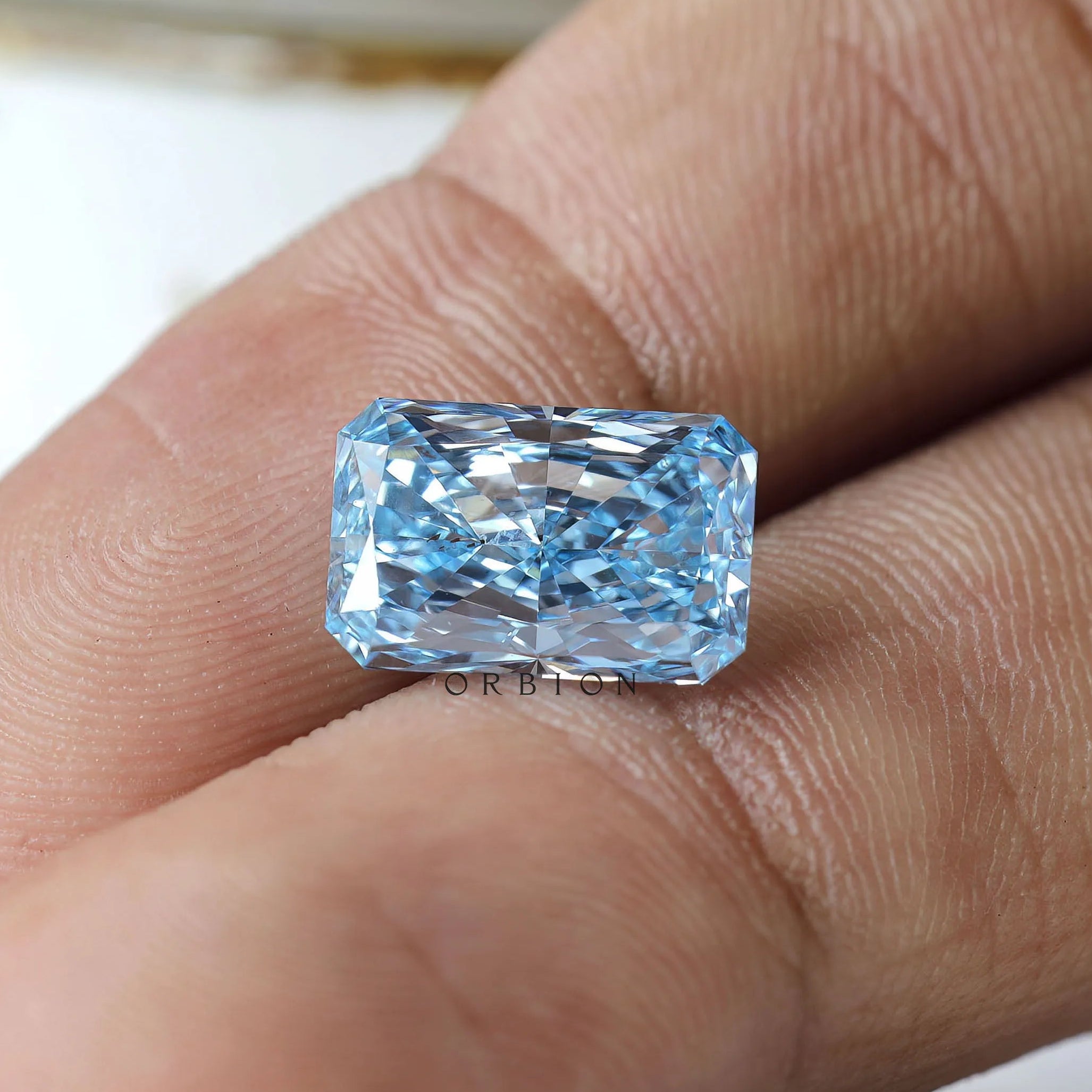 Blue radiant brilliant loose diamond shown on fingertip
