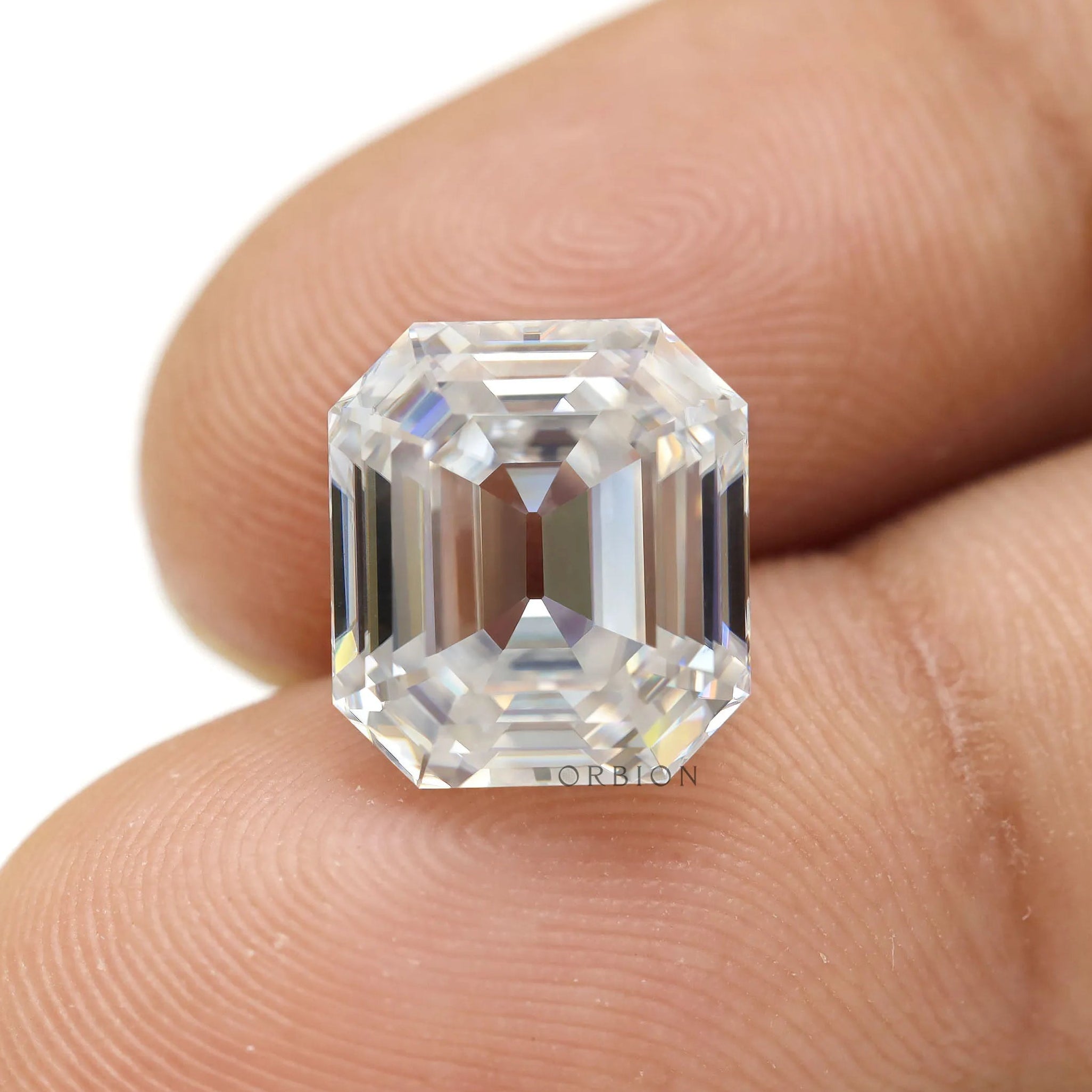 Loose emerald step cut moissanite displayed on fingertips close-up