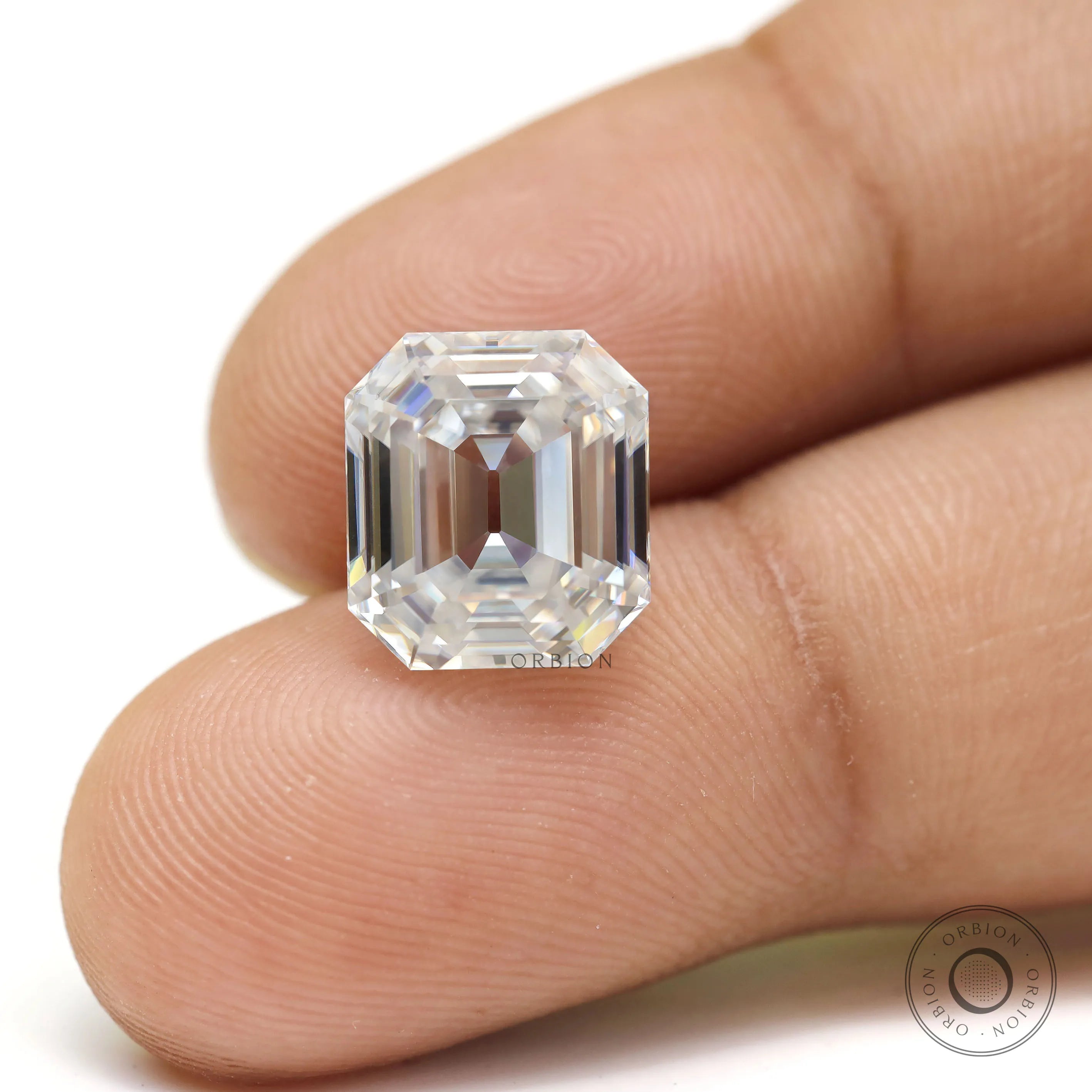 Loose emerald step cut moissanite displayed on fingertips close-up