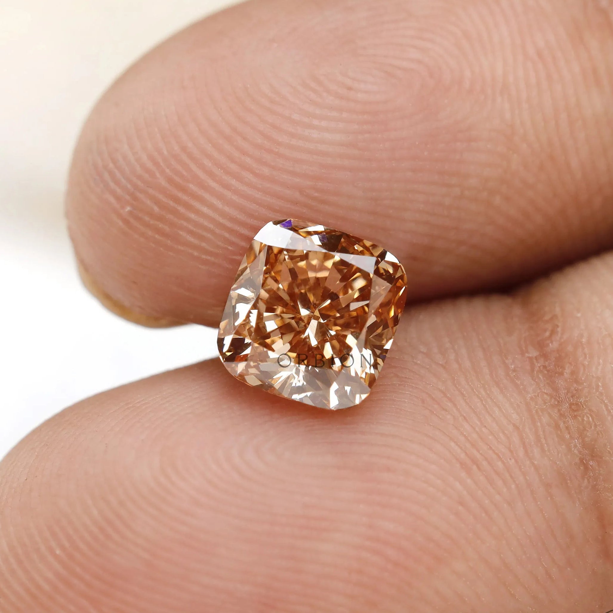Close fingertip view of fancy orange cushion lab diamond