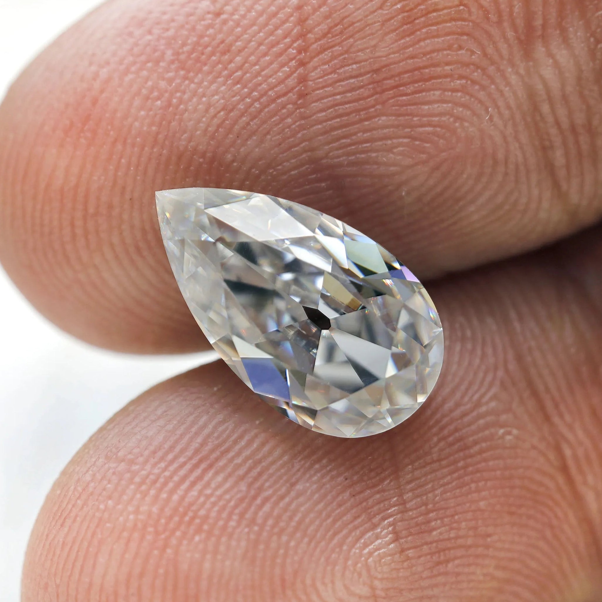 Pear loose moissanite placed on fingertips for size