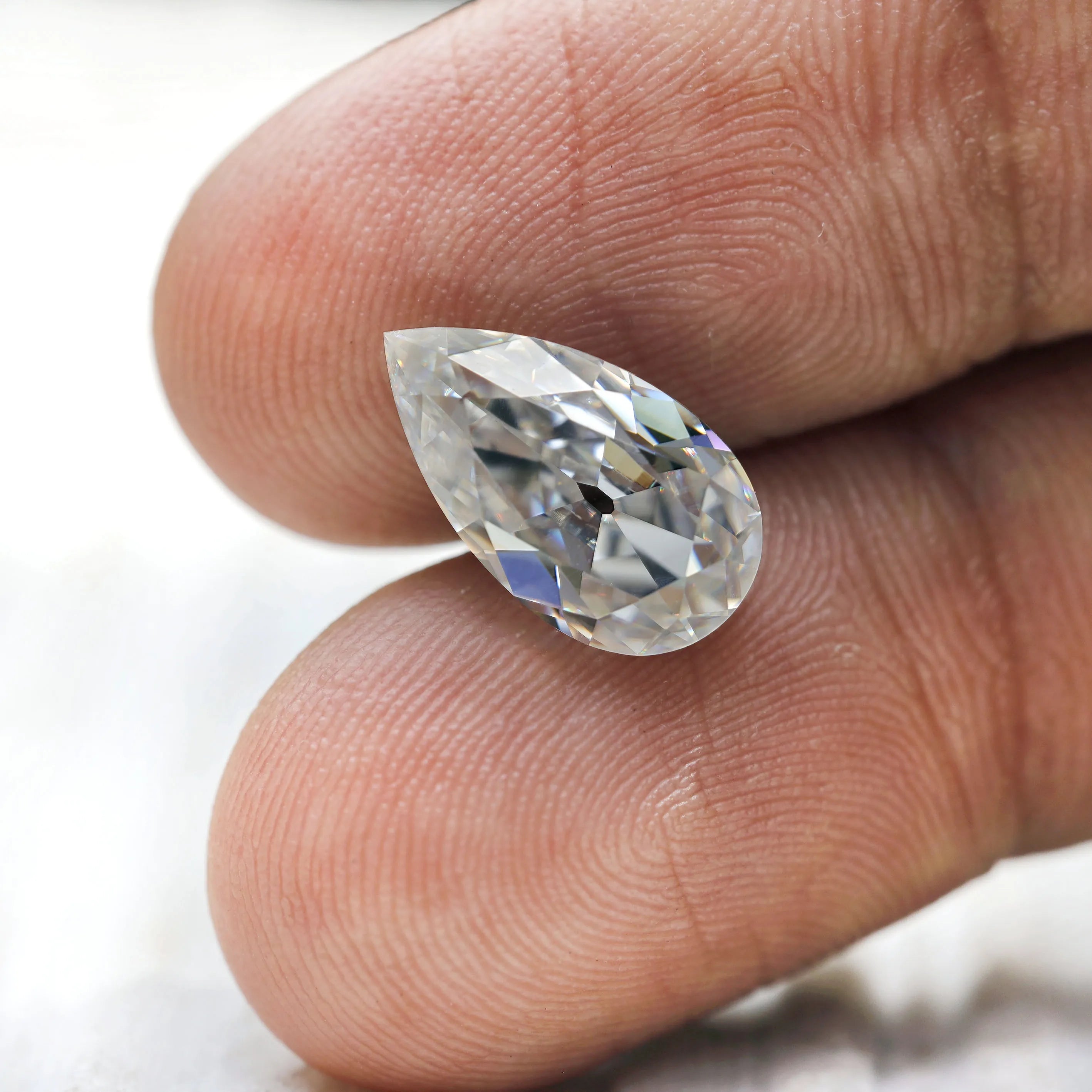 Pear loose moissanite placed on fingertips for size