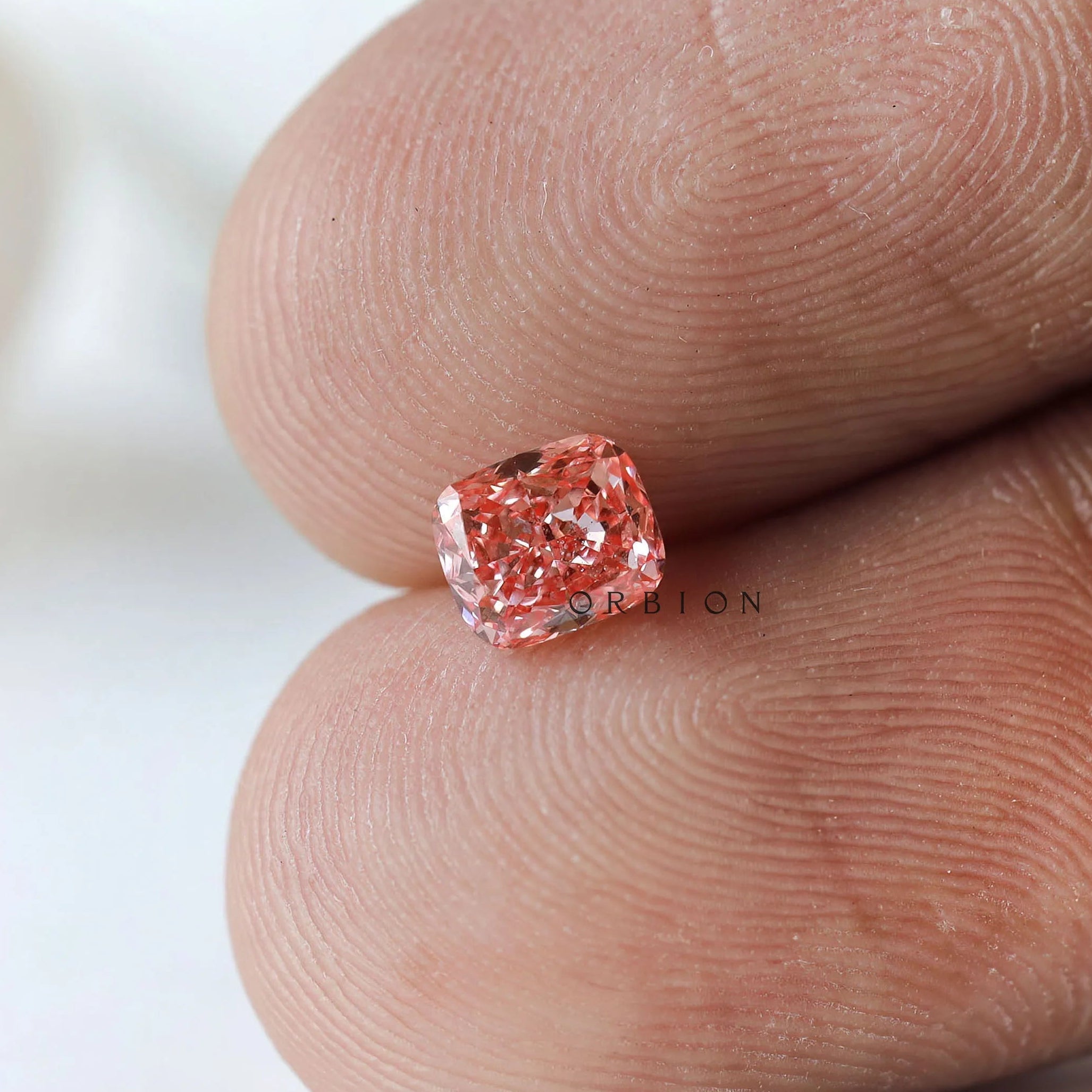 Vivid pink cushion lab diamond displayed on fingertip