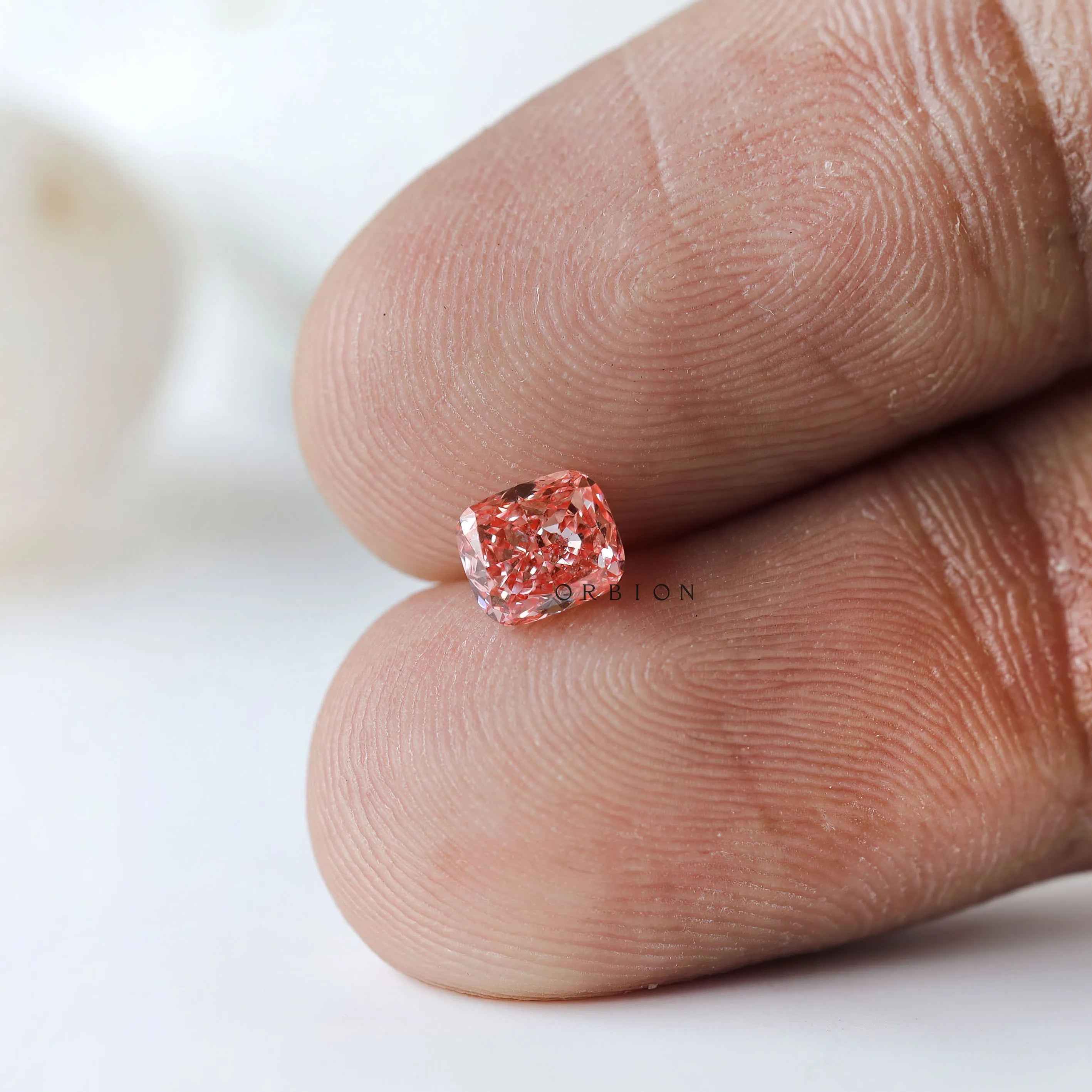 Vivid pink cushion lab diamond displayed on fingertip