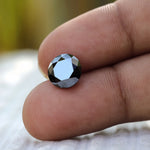 Round black Moissanite in hand showcasing its cut between finger held 
