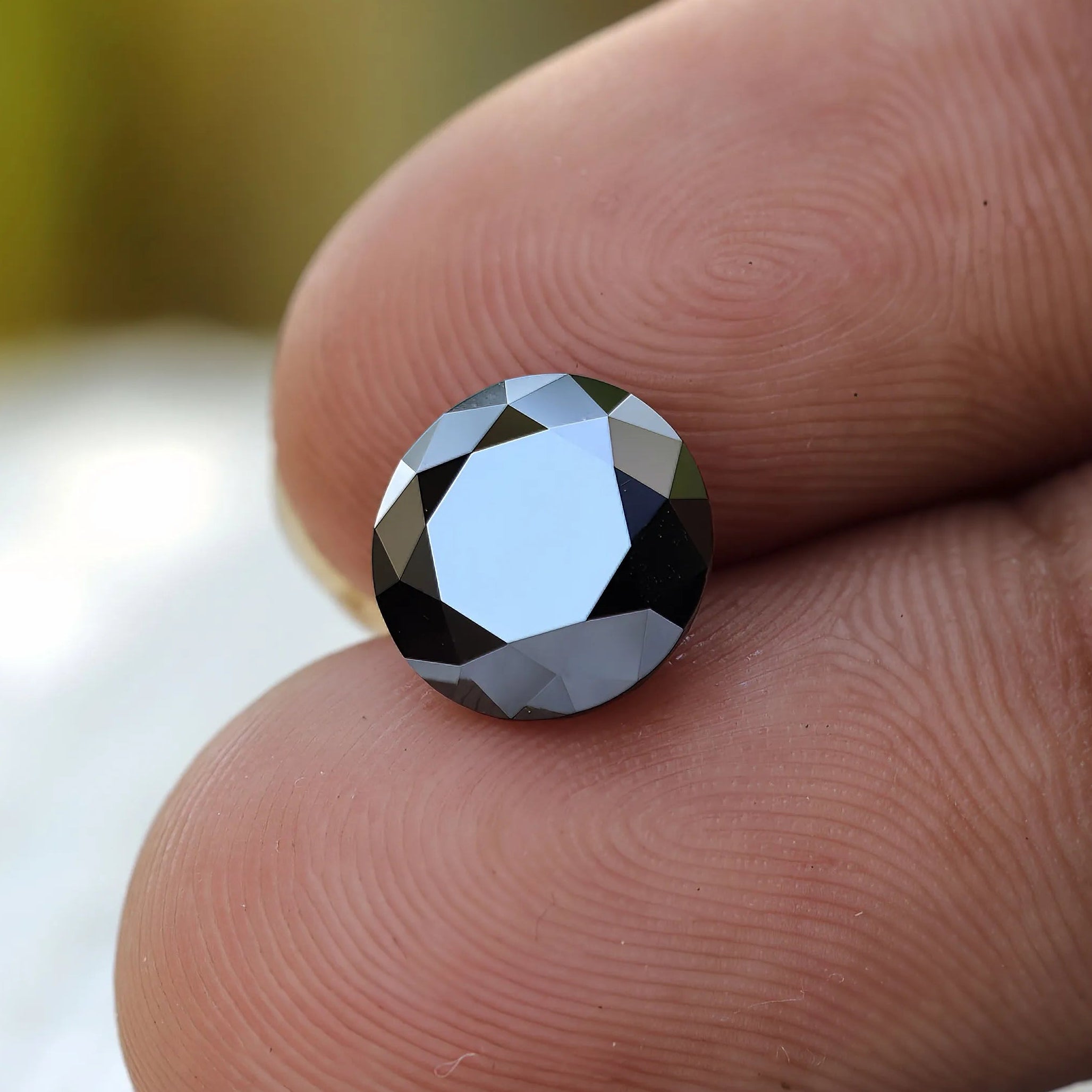 Round black Moissanite in hand showcasing its cut between finger held 