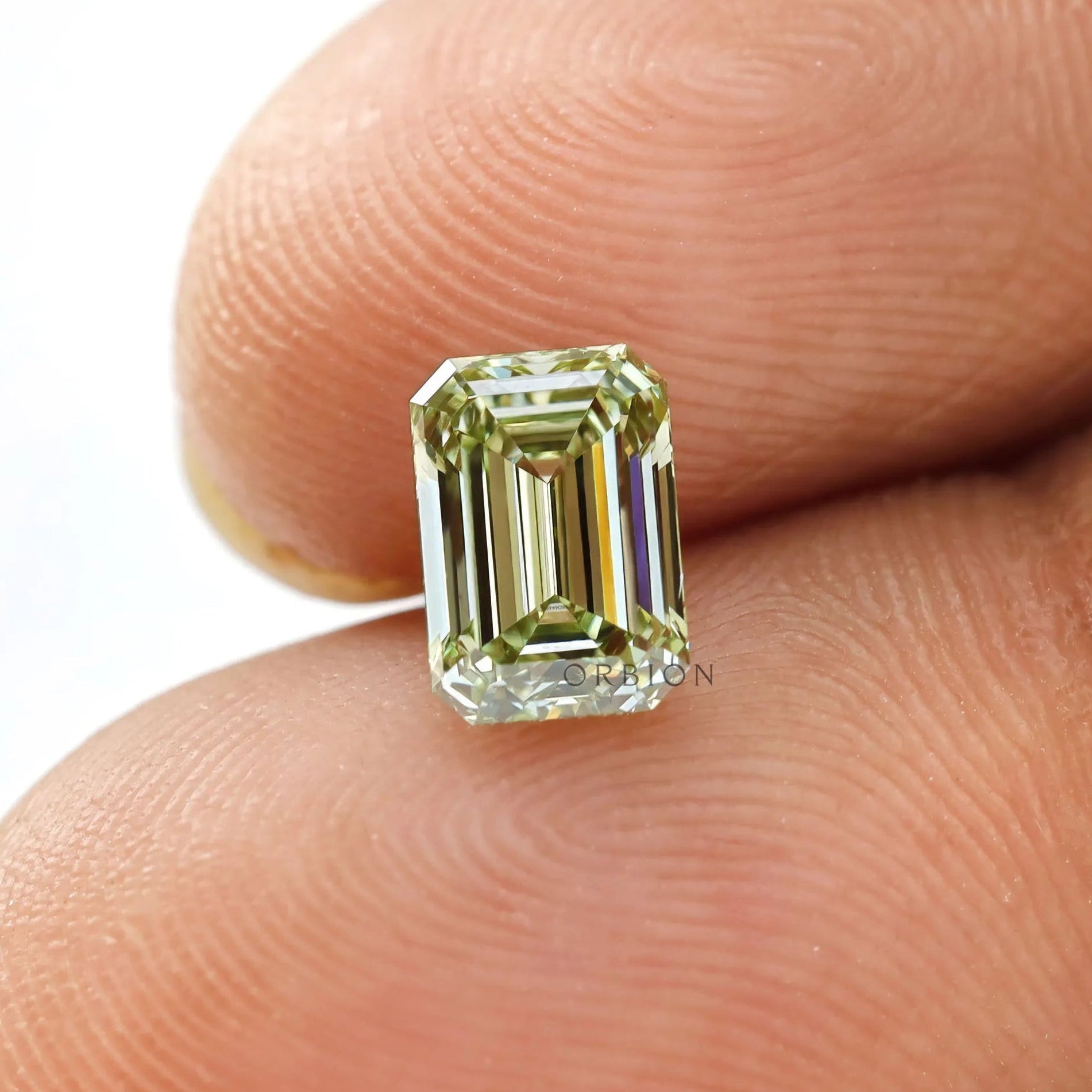 Fancy green emerald lab diamond shown on fingertip