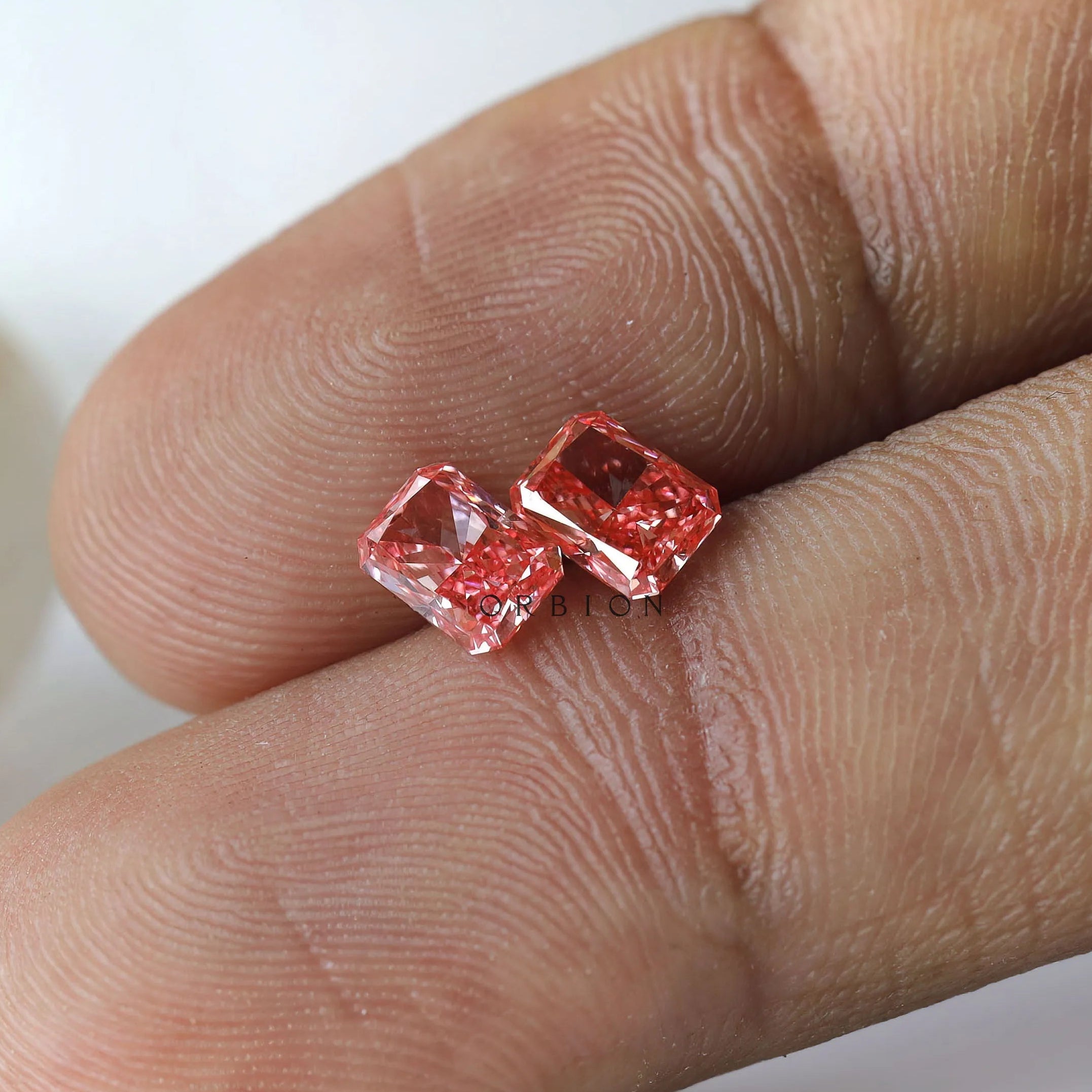 Macro fingertip view of vivid pink radiant diamond pair