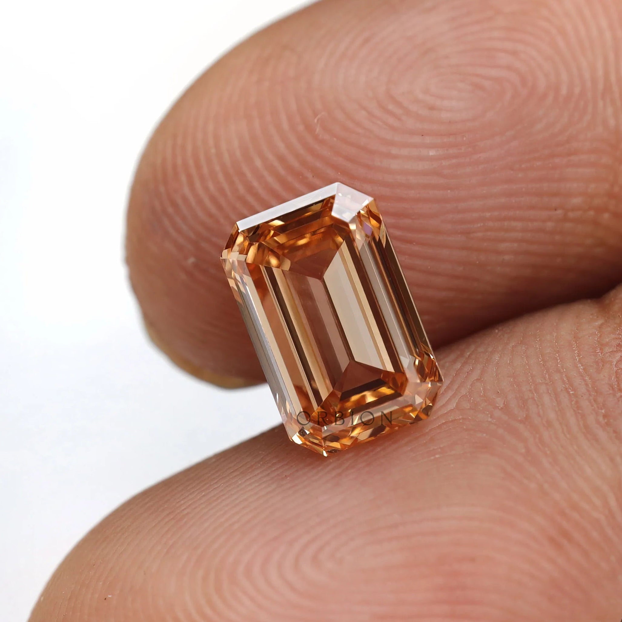 Close fingertip view of orange emerald lab diamond