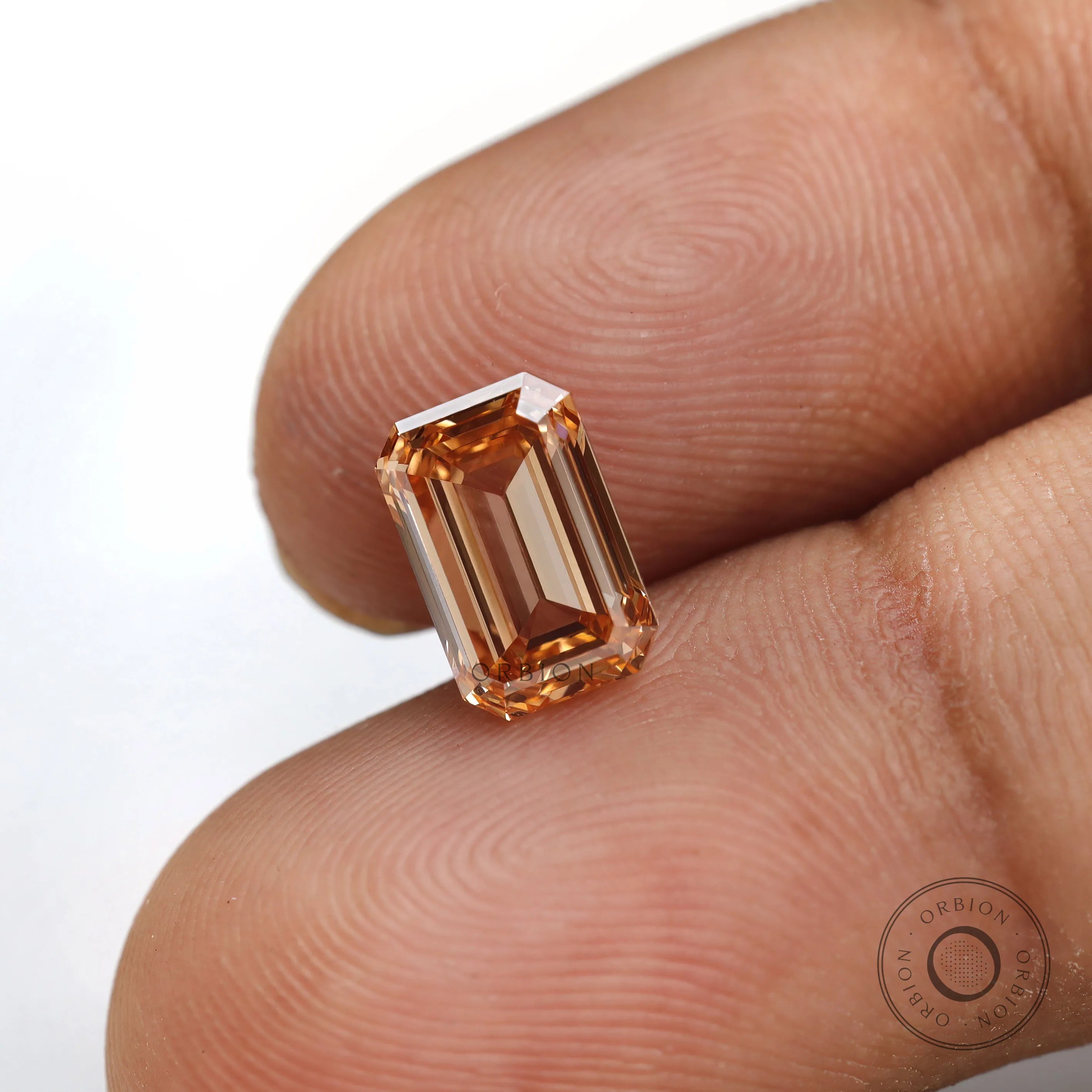 Close fingertip view of orange emerald lab diamond