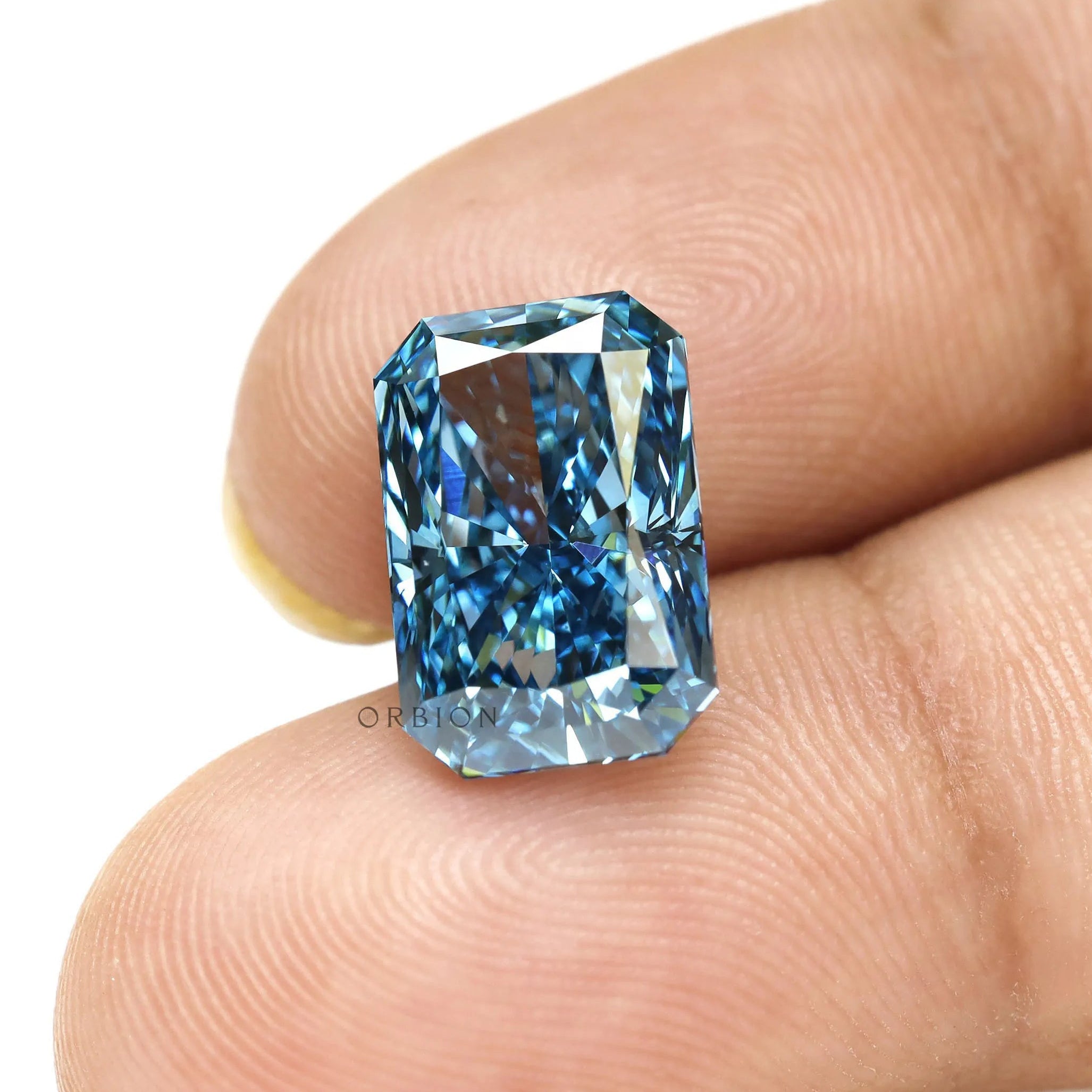 Fancy vivid blue radiant lab diamond shown on fingertips