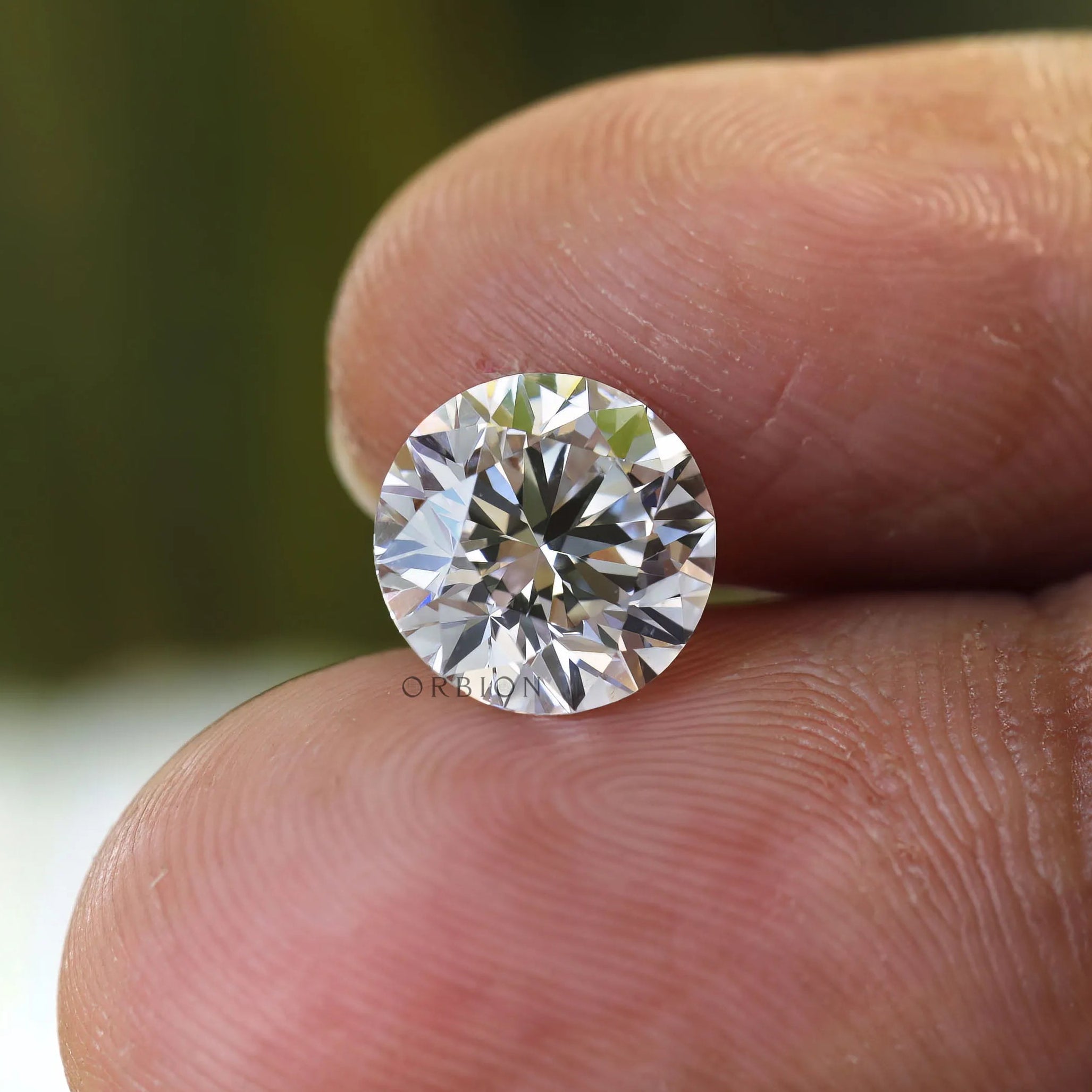Brilliant cut round lab diamond held on fingertips