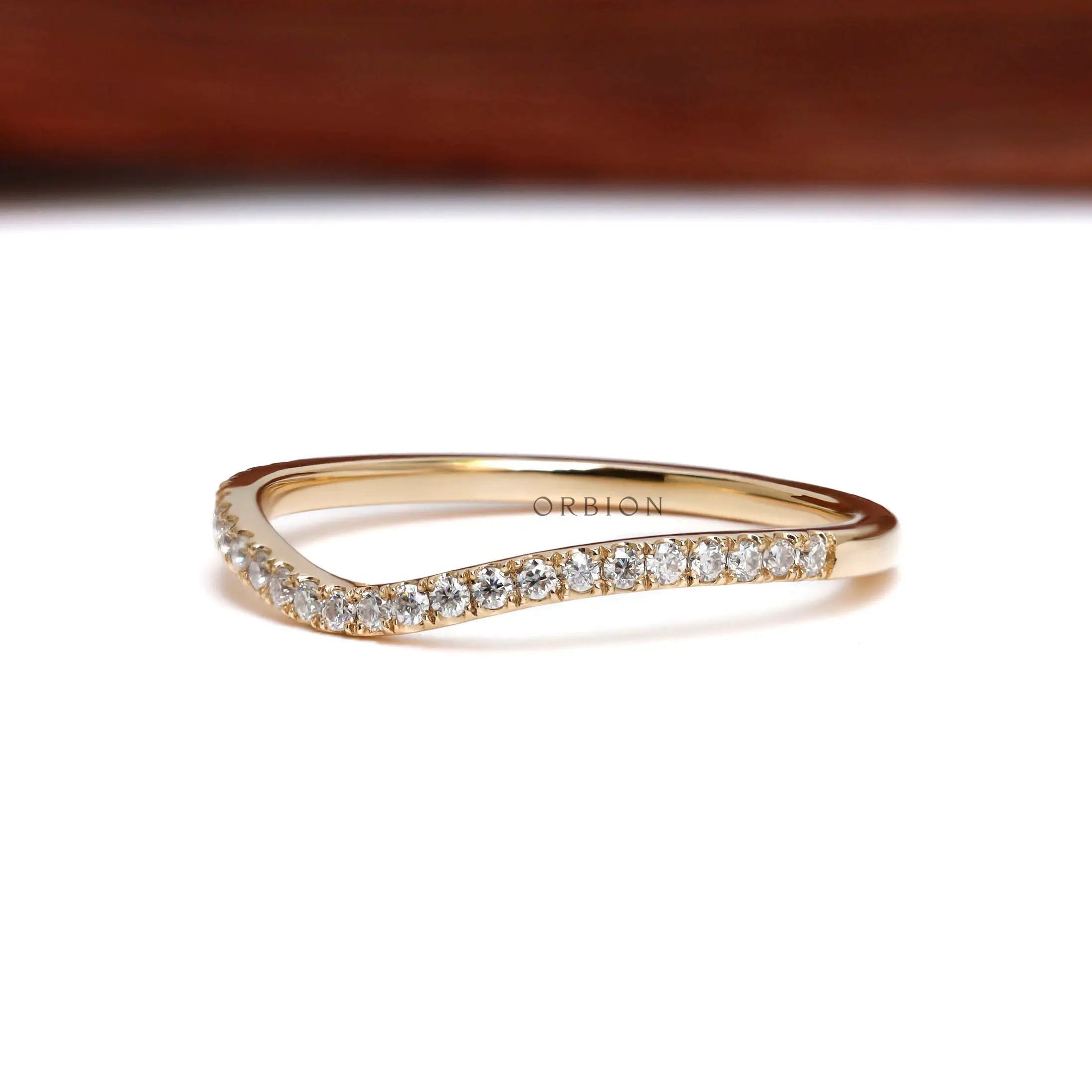 Front angled view of curved moissanite wedding band in yellow gold