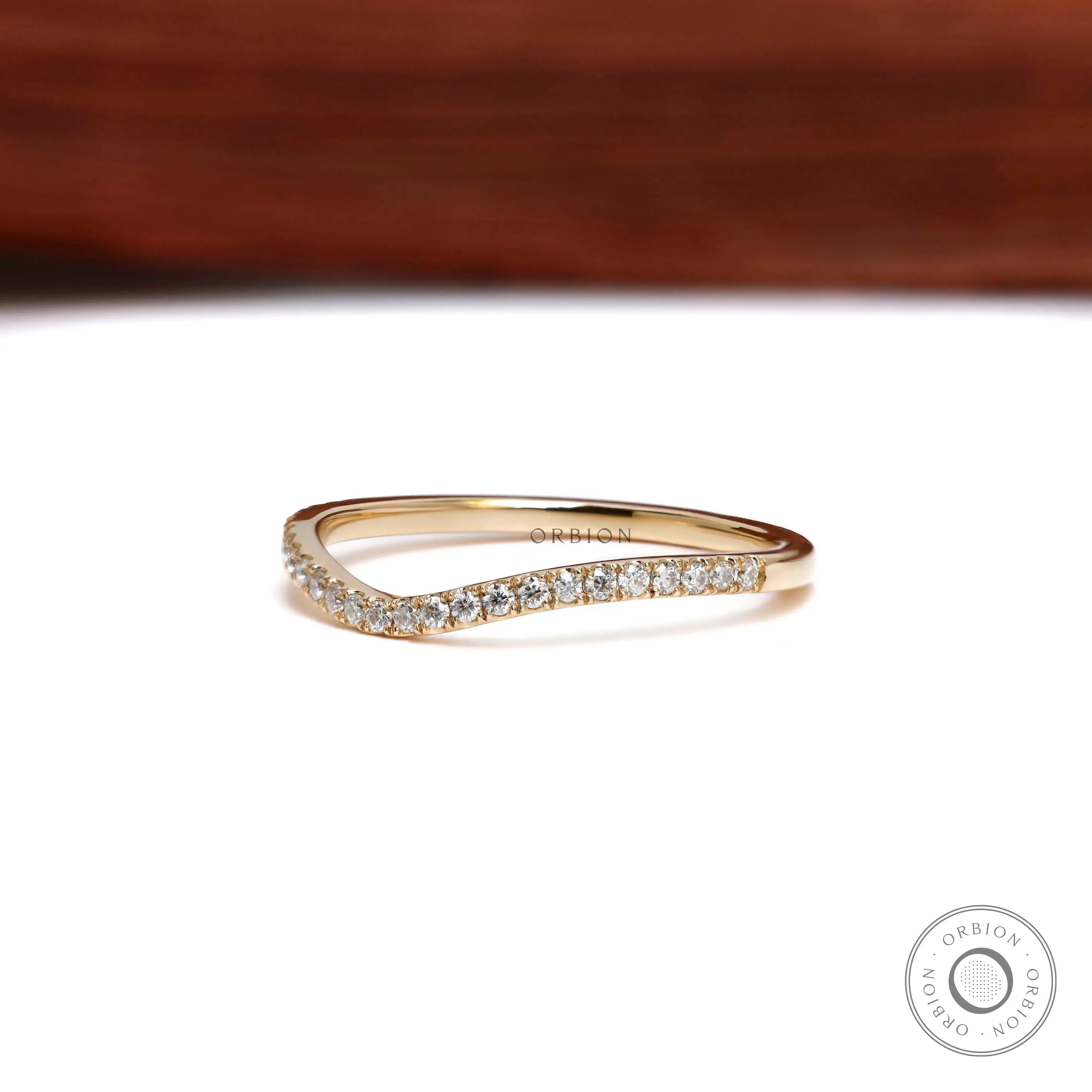 Front angled view of curved moissanite wedding band in yellow gold