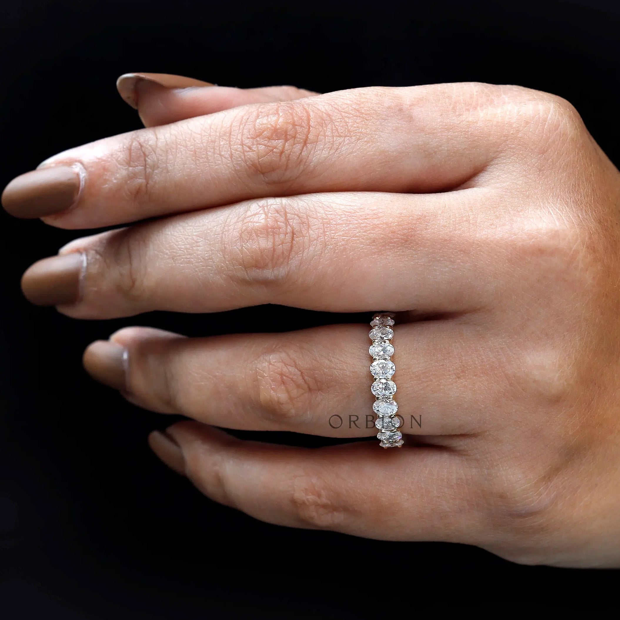 Oval moissanite half eternity ring held by hand with prong detail
