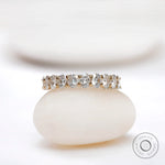 Oval moissanite half eternity band displayed on a smooth white stone