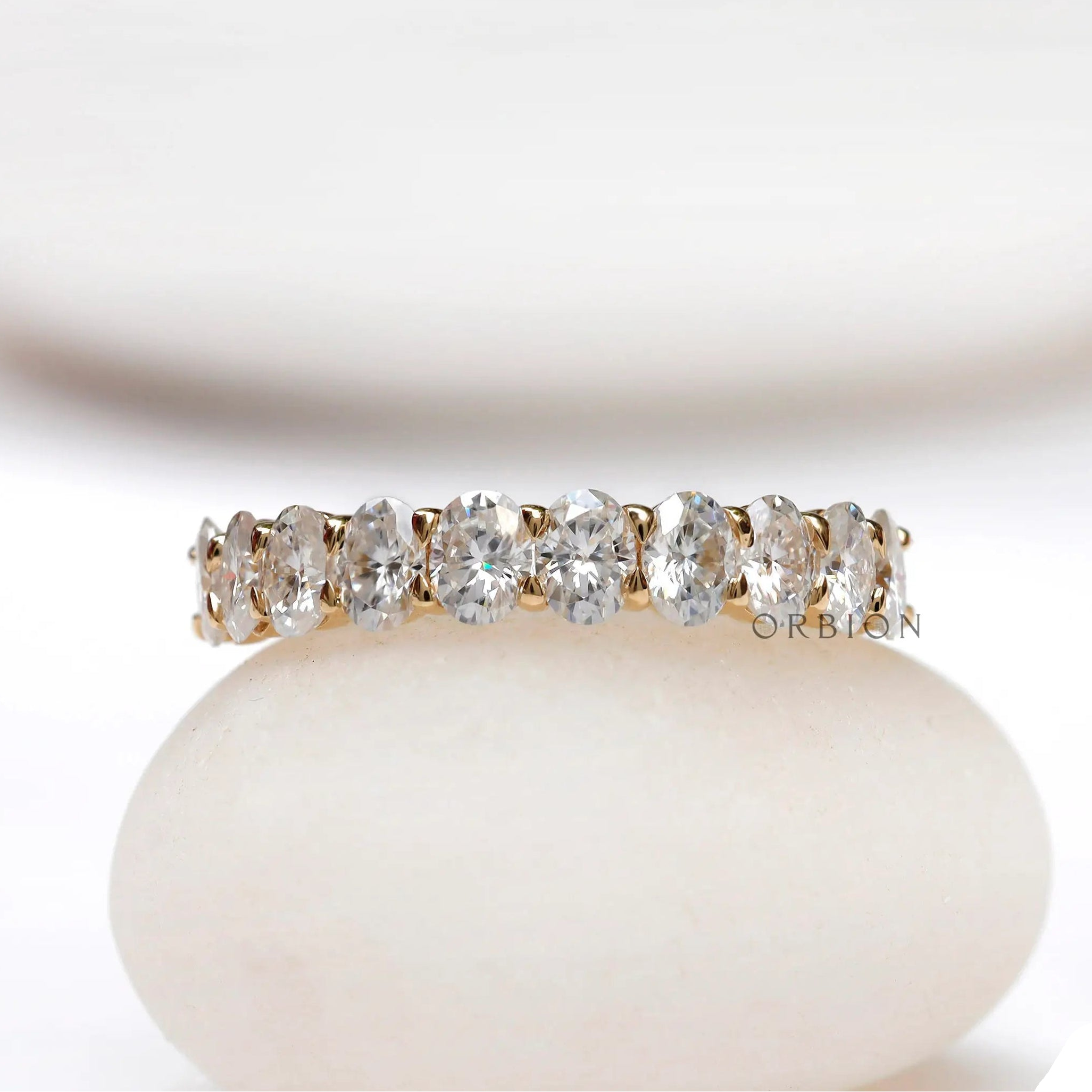 Oval moissanite half eternity band displayed on a smooth white stone
