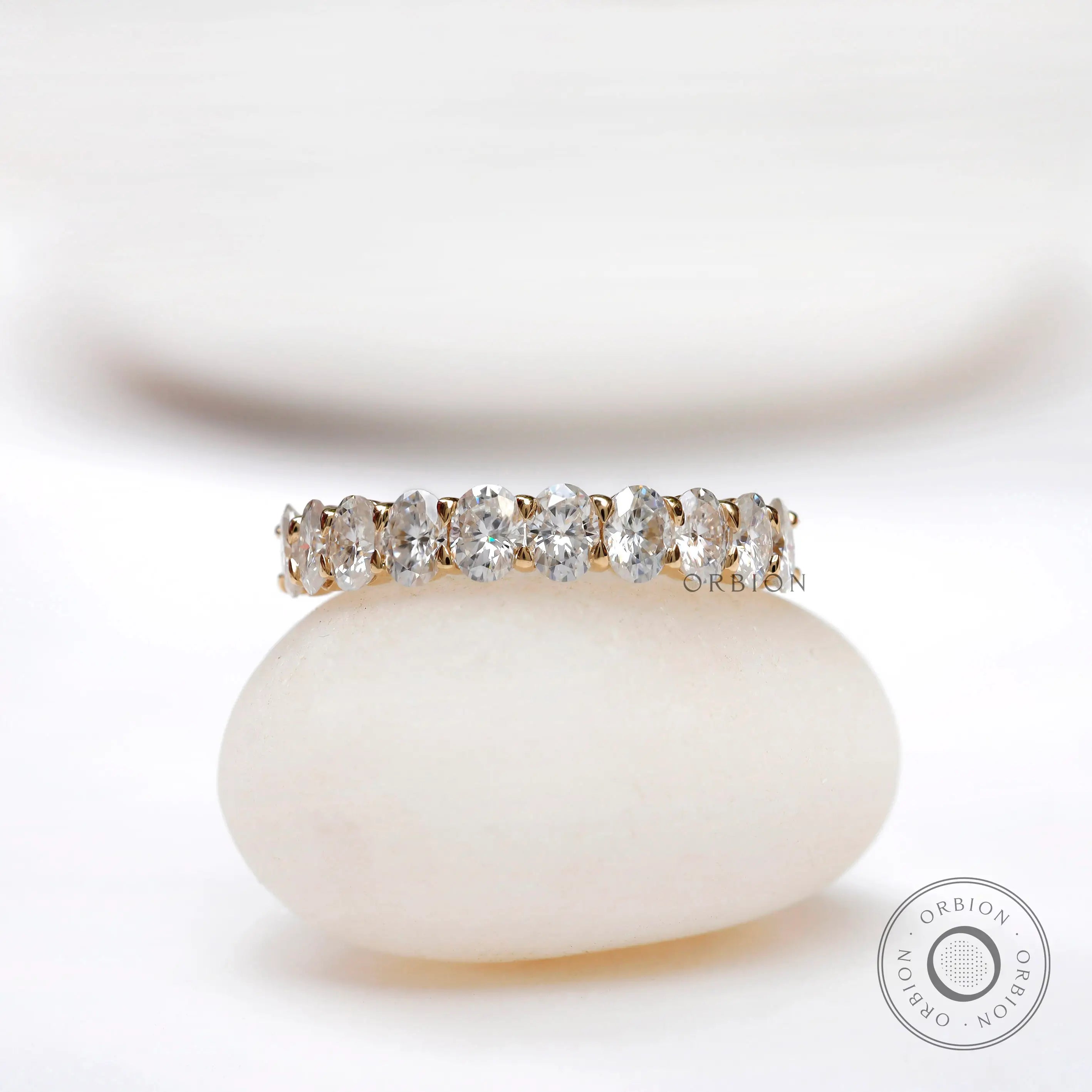 Oval moissanite half eternity band displayed on a smooth white stone