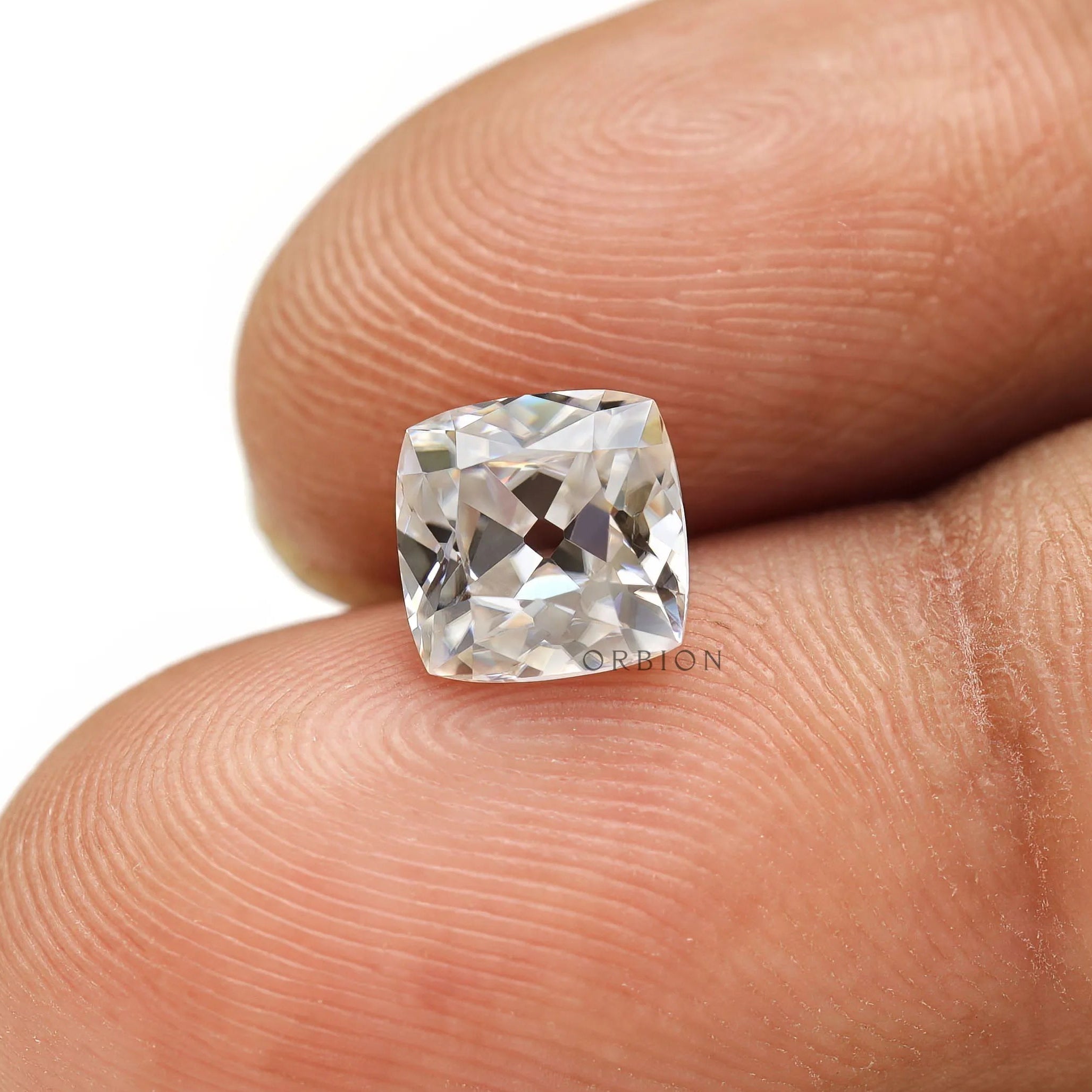 Cushion moissanite gemstone shown on fingertip