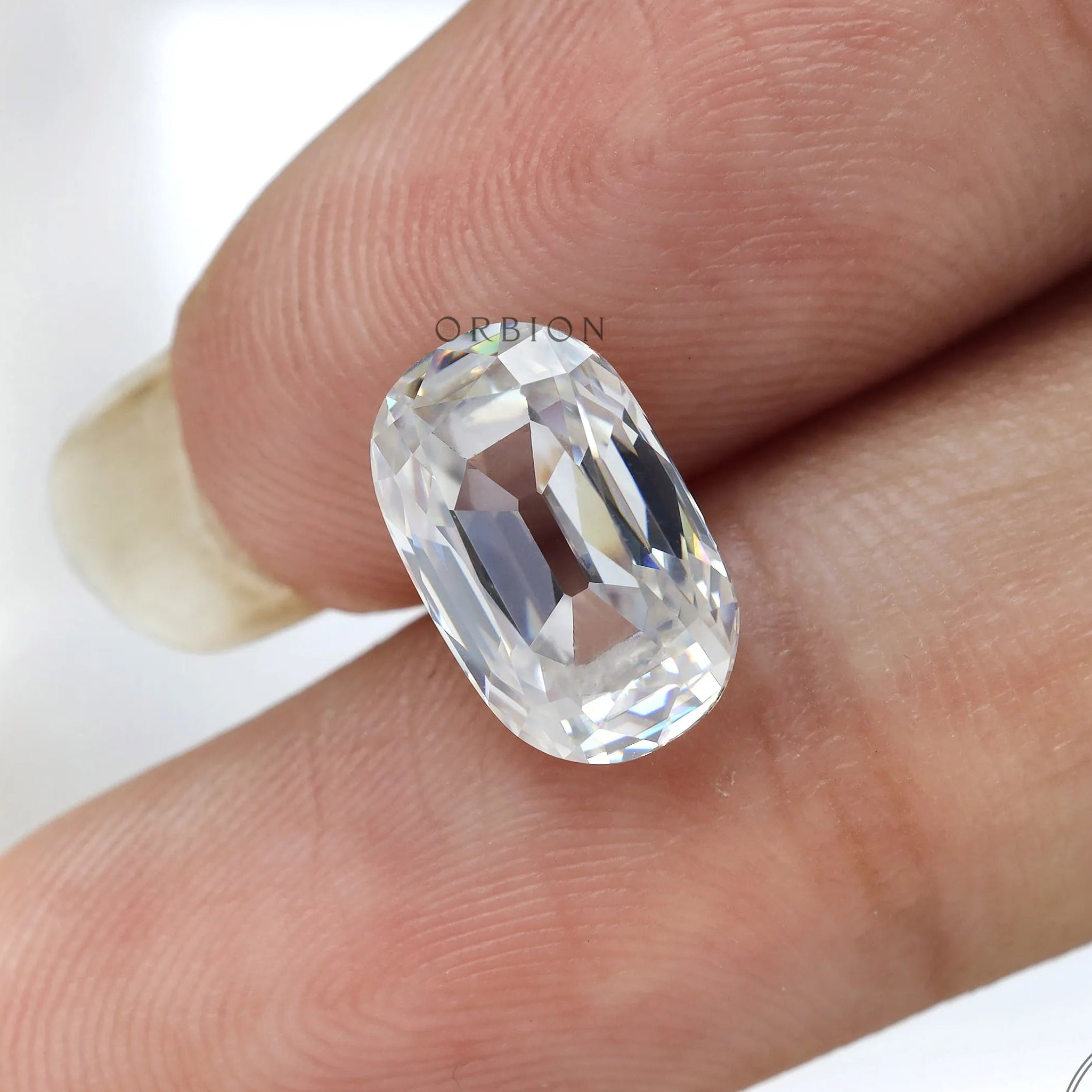 loose elongated cushion moissanite placed on fingertip close detail